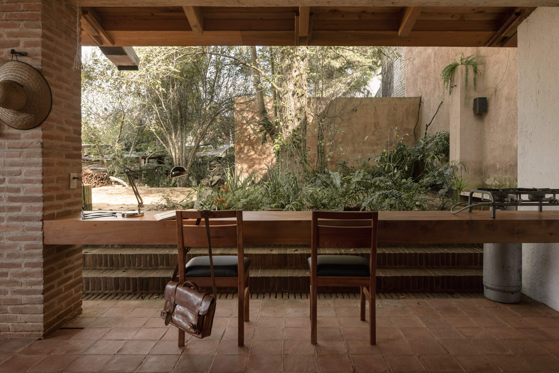Step into Casa Amona’s courtyard in Chiapas, México, where an existing ash tree shades a brick fire pit and a covered workspace opens onto the planting.