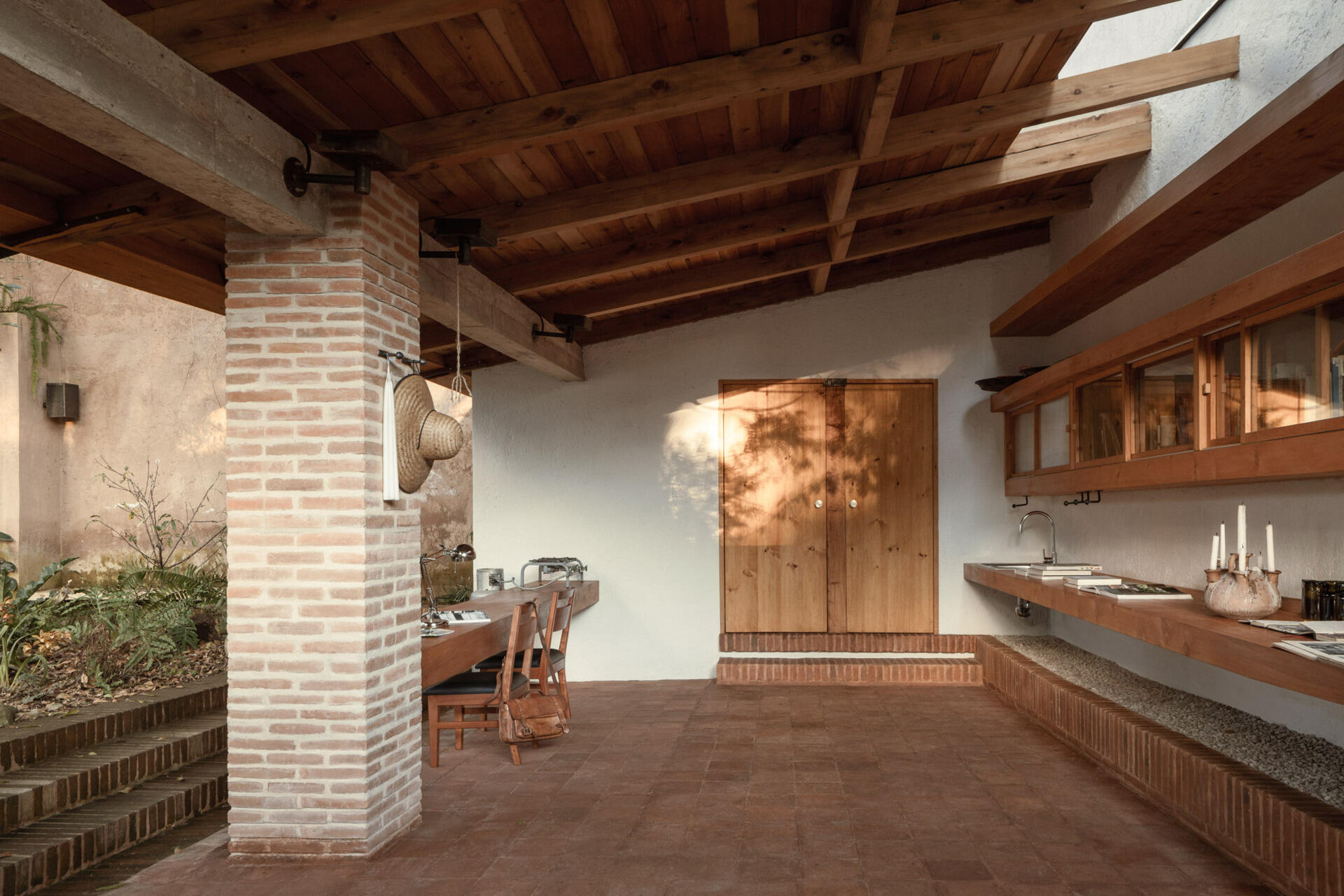 Step into Casa Amona’s courtyard in Chiapas, México, where an existing ash tree shades a brick fire pit and a covered workspace opens onto the planting.
