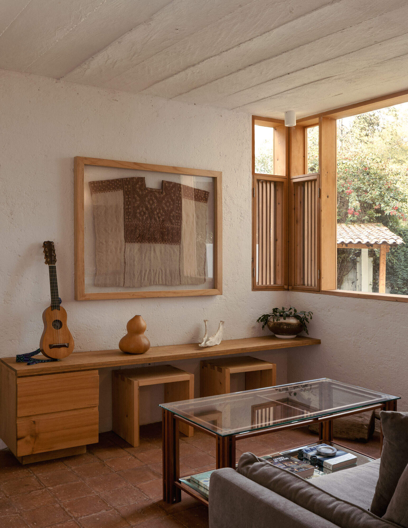 See inside Casa Amona’s living room, where clay tile floors, timber details and a corner window create a warm, compact space designed to adapt over time.