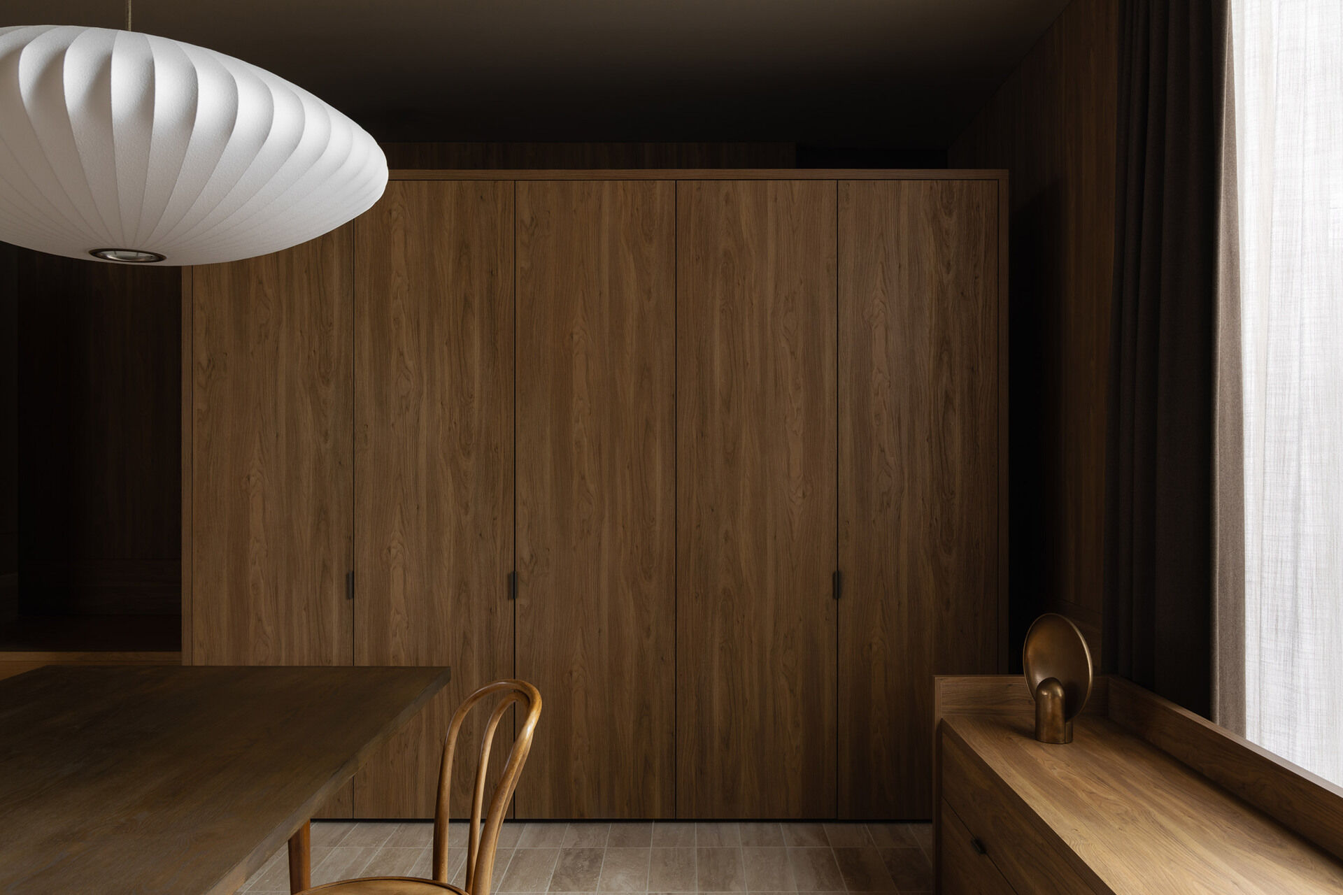 Warm timber cabinetry, bentwood chairs, a dark dining table and an oversized white pendant define Casa Piva’s dining area, with the larger internal courtyard bringing daylight and planting into the living spaces.