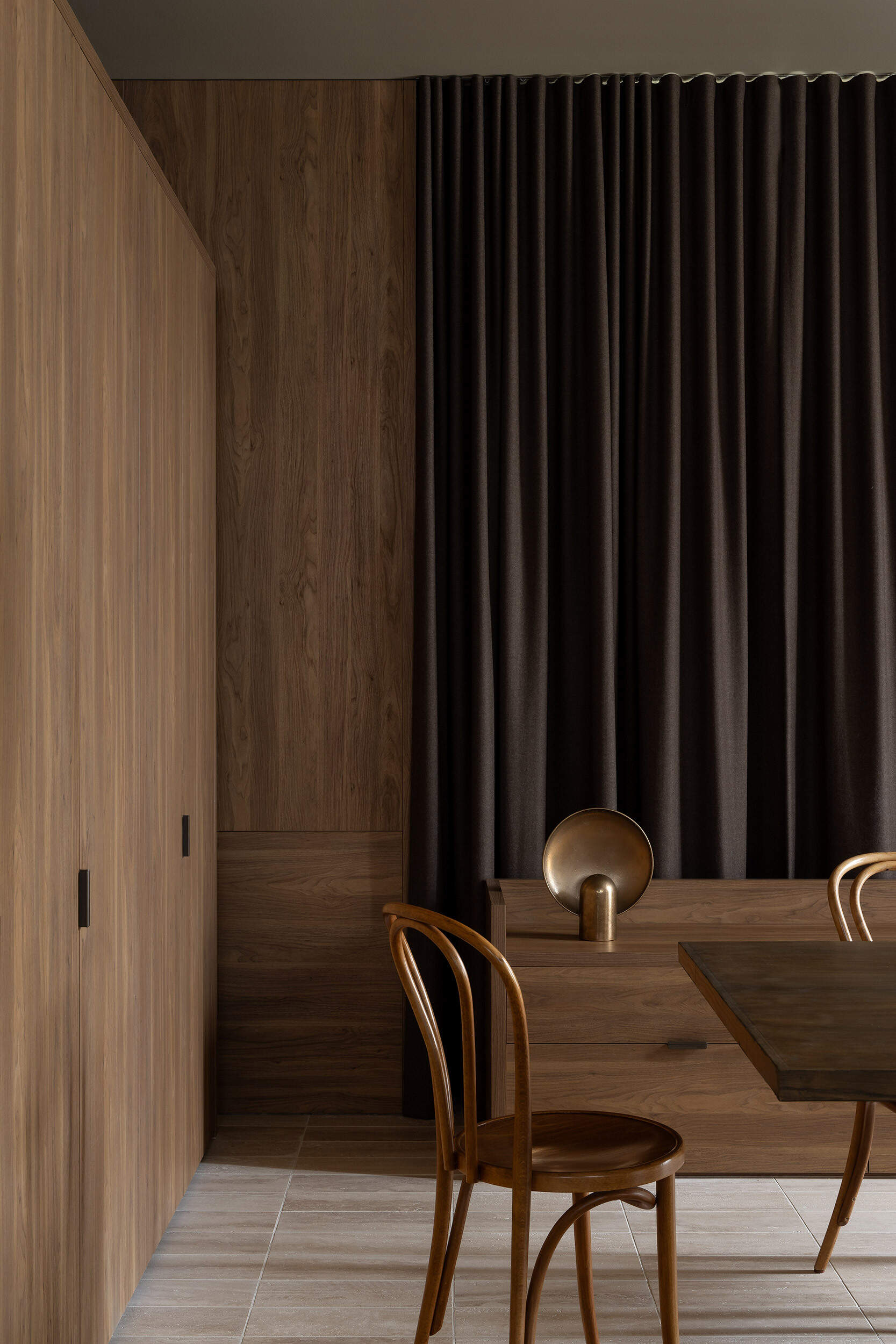 Warm timber cabinetry, bentwood chairs, a dark dining table and an oversized white pendant define Casa Piva’s dining area, with the larger internal courtyard bringing daylight and planting into the living spaces.