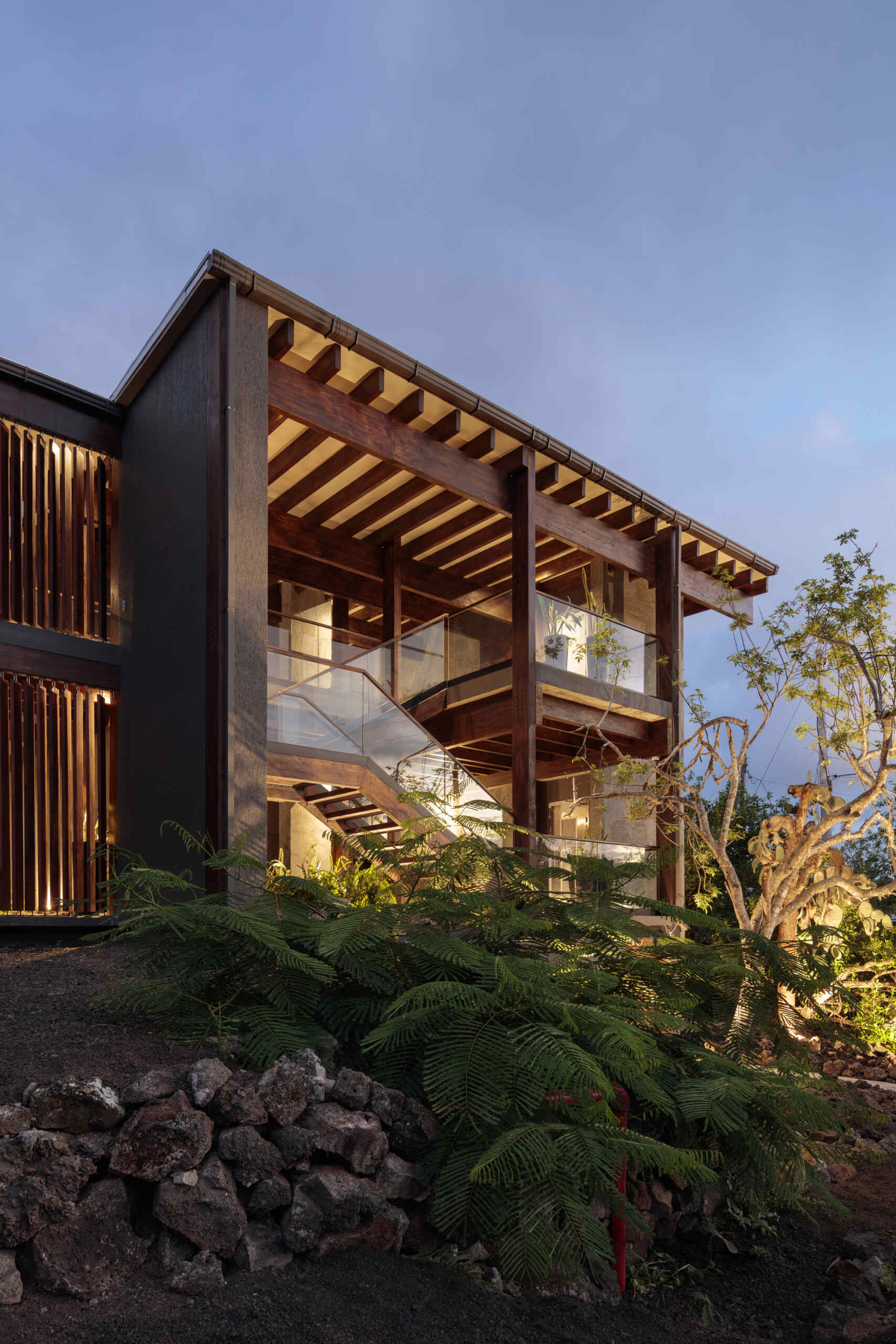 Explore the Finch Bay Galápagos Hotel expansion near Puerto Ayora, Ecuador, by Alfredo Ribadeneira Arquitectos. Prefabricated teak construction, deep roof overhangs, glass-fronted terraces, and neutral guest spaces frame views of trees and volcanic rock.