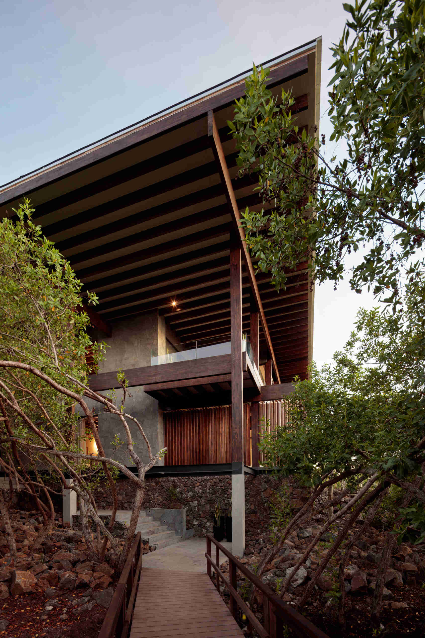 Explore the Finch Bay Galápagos Hotel expansion near Puerto Ayora, Ecuador, by Alfredo Ribadeneira Arquitectos. Prefabricated teak construction, deep roof overhangs, glass-fronted terraces, and neutral guest spaces frame views of trees and volcanic rock.