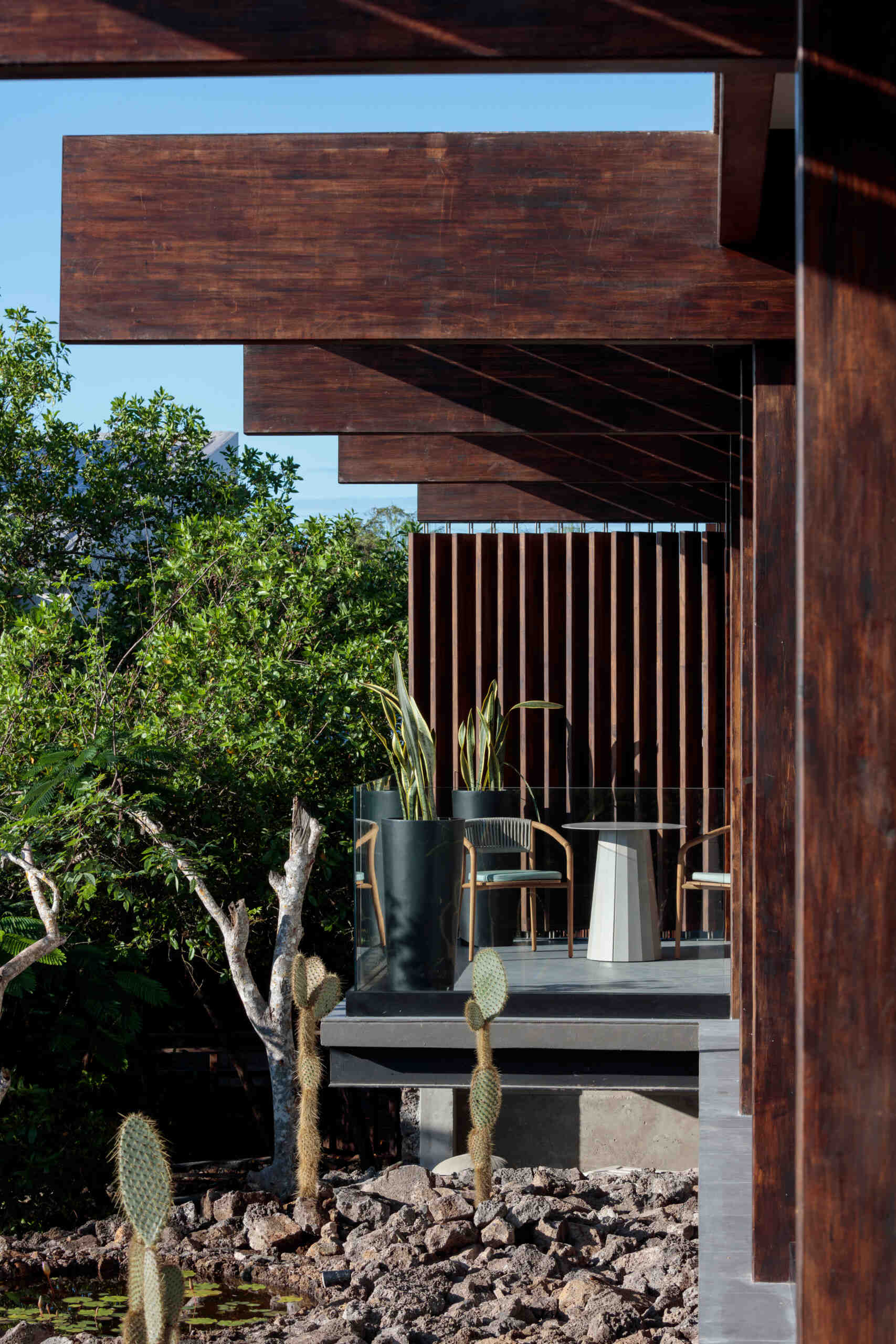 Explore the Finch Bay Galápagos Hotel expansion near Puerto Ayora, Ecuador, by Alfredo Ribadeneira Arquitectos. Prefabricated teak construction, deep roof overhangs, glass-fronted terraces, and neutral guest spaces frame views of trees and volcanic rock.