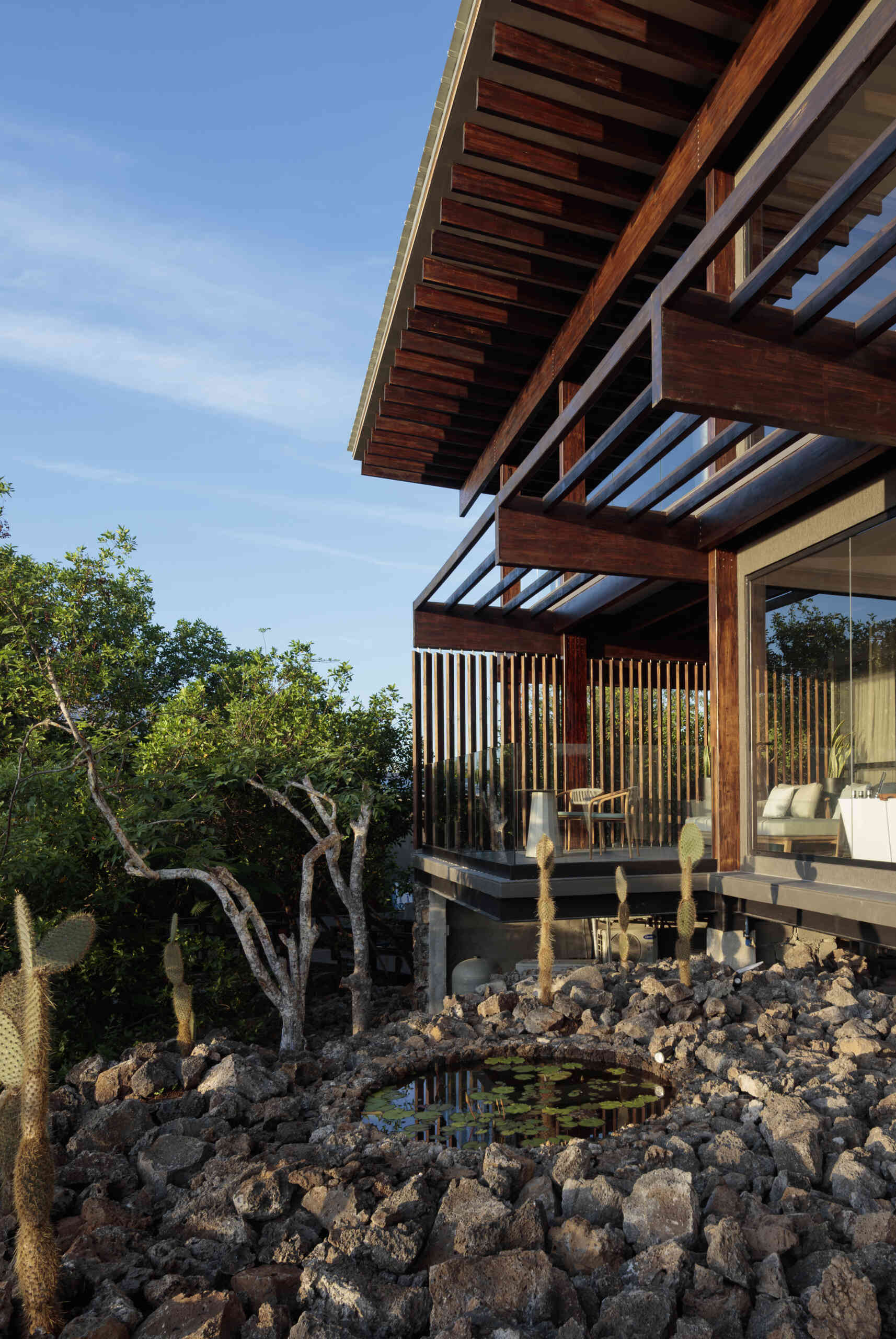Explore the Finch Bay Galápagos Hotel expansion near Puerto Ayora, Ecuador, by Alfredo Ribadeneira Arquitectos. Prefabricated teak construction, deep roof overhangs, glass-fronted terraces, and neutral guest spaces frame views of trees and volcanic rock.