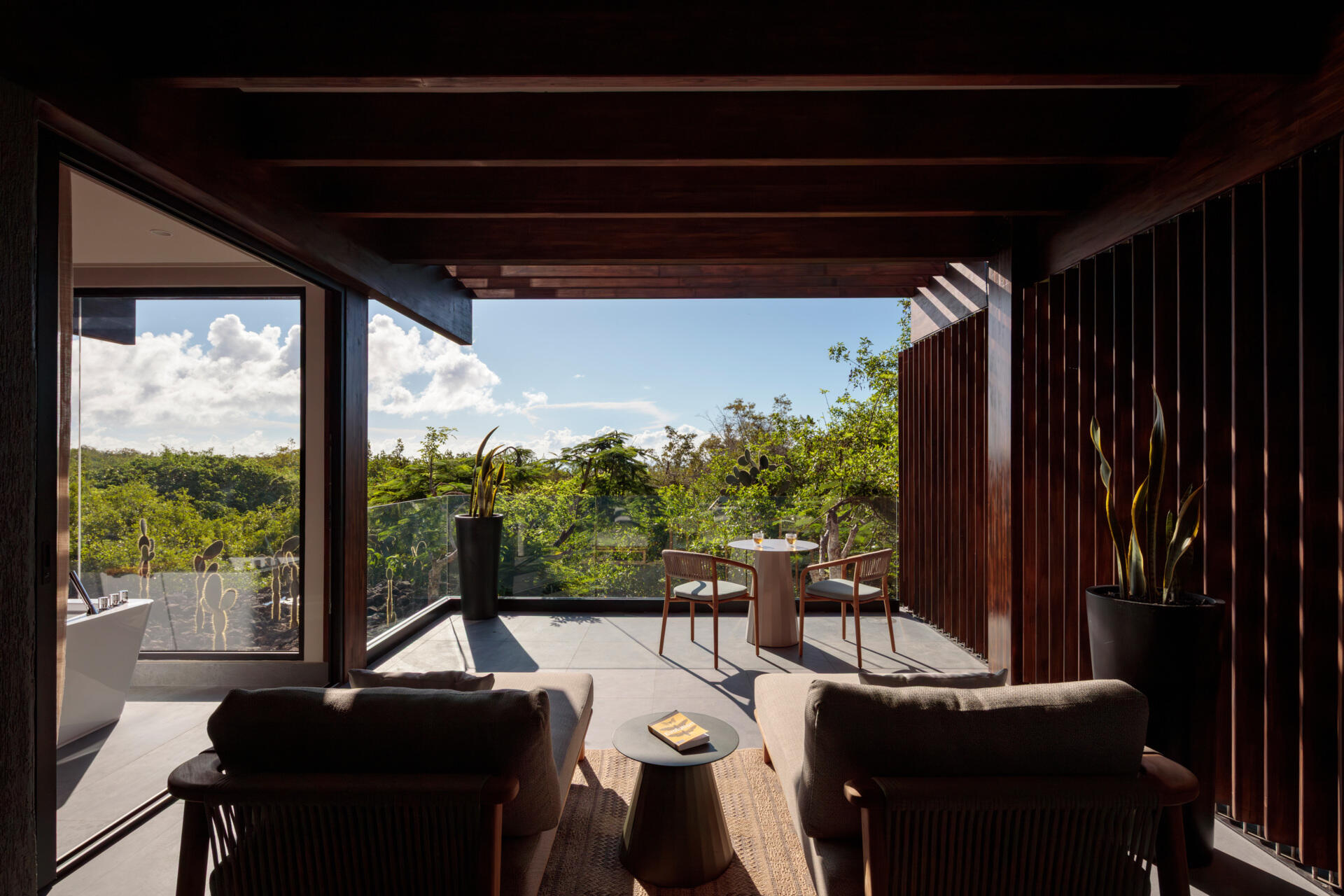 Explore the Finch Bay Galápagos Hotel expansion near Puerto Ayora, Ecuador, by Alfredo Ribadeneira Arquitectos. Prefabricated teak construction, deep roof overhangs, glass-fronted terraces, and neutral guest spaces frame views of trees and volcanic rock.