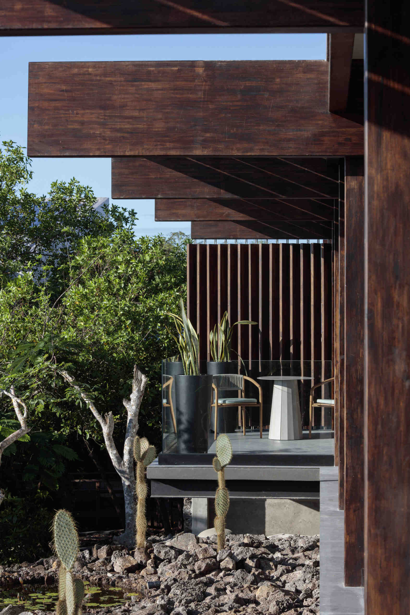 Explore the Finch Bay Galápagos Hotel expansion near Puerto Ayora, Ecuador, by Alfredo Ribadeneira Arquitectos. Prefabricated teak construction, deep roof overhangs, glass-fronted terraces, and neutral guest spaces frame views of trees and volcanic rock.
