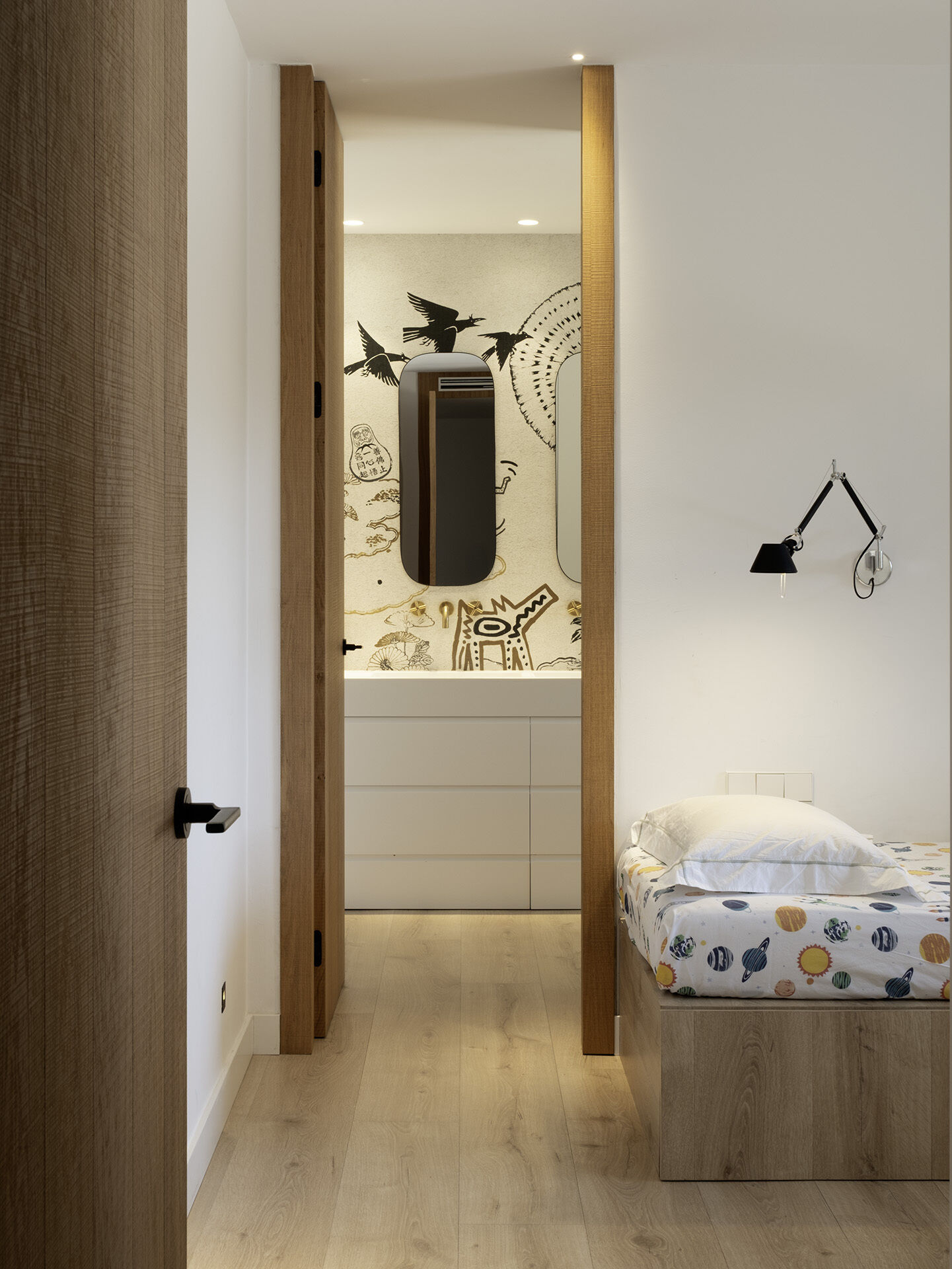 A playful illustrated wall treatment gives this guest bathroom a completely different character from the rest of the home. Black-and-white graphics wrap around the bathtub, while pale timber flooring and simple white fittings keep the space balanced.
