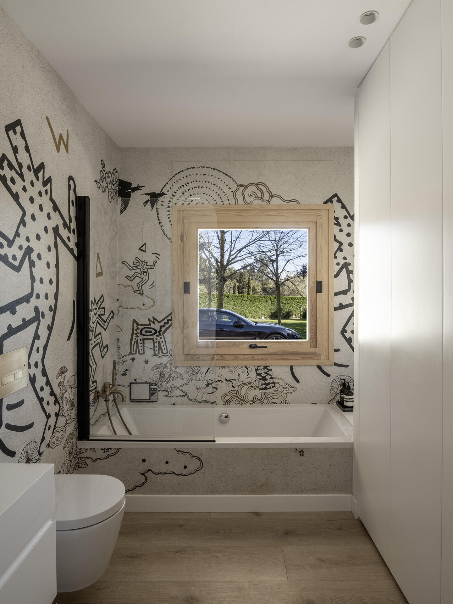A playful illustrated wall treatment gives this guest bathroom a completely different character from the rest of the home. Black-and-white graphics wrap around the bathtub, while pale timber flooring and simple white fittings keep the space balanced.