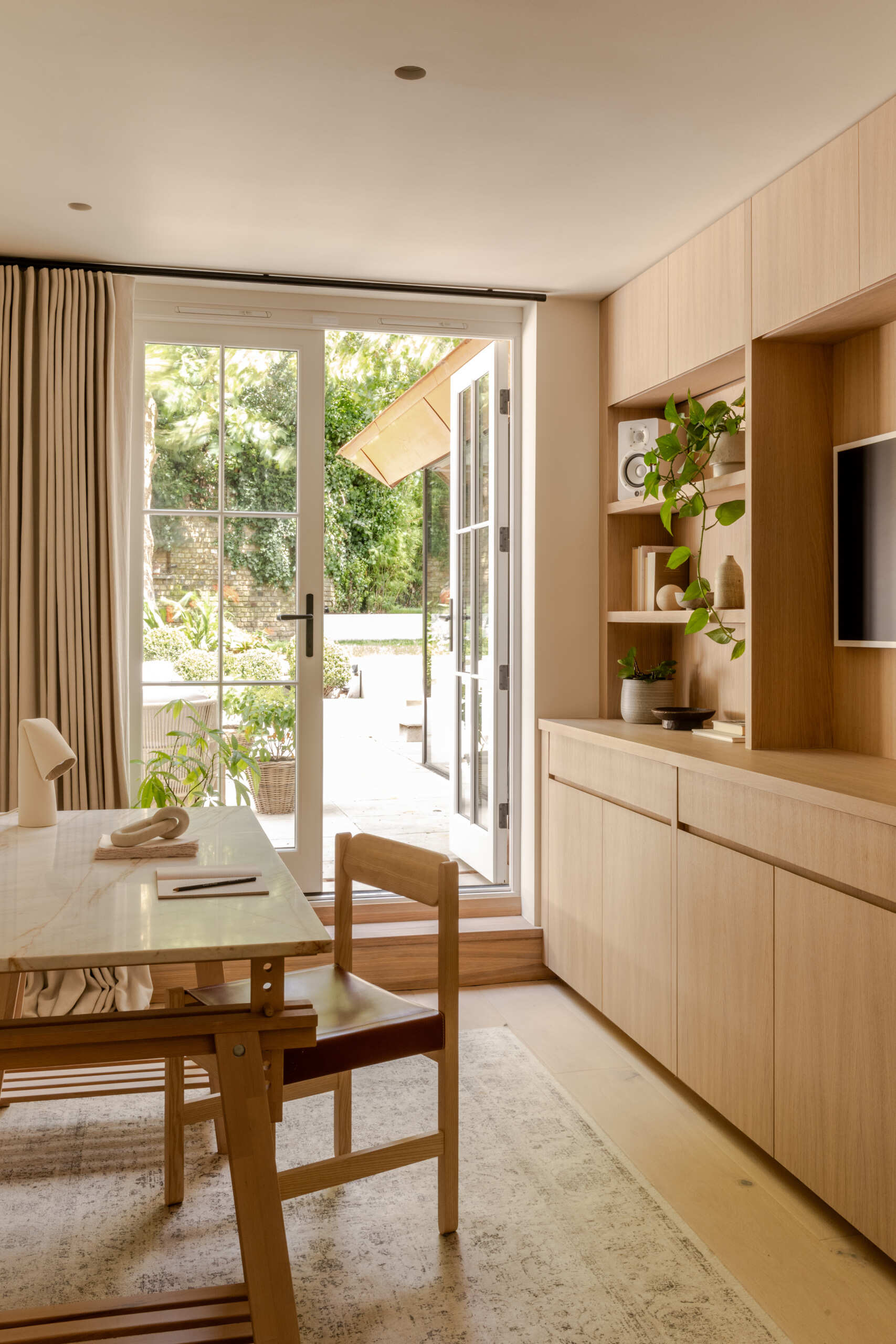 See the home office and media space at Thirsk Cottage, featuring warm oak built-ins, garden-facing French doors, open shelving and integrated DJ equipment.