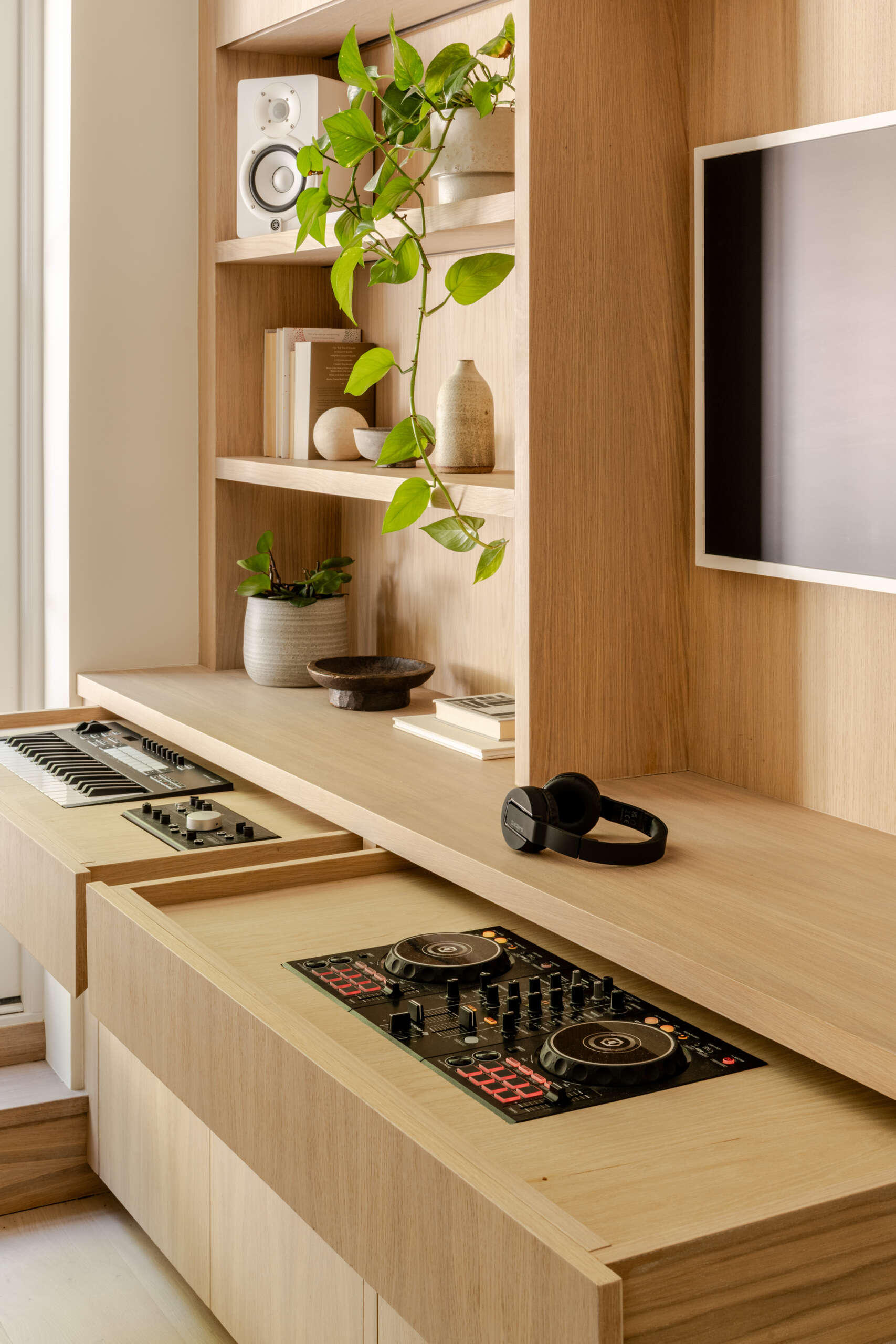 See the home office and media space at Thirsk Cottage, featuring warm oak built-ins, garden-facing French doors, open shelving and integrated DJ equipment.