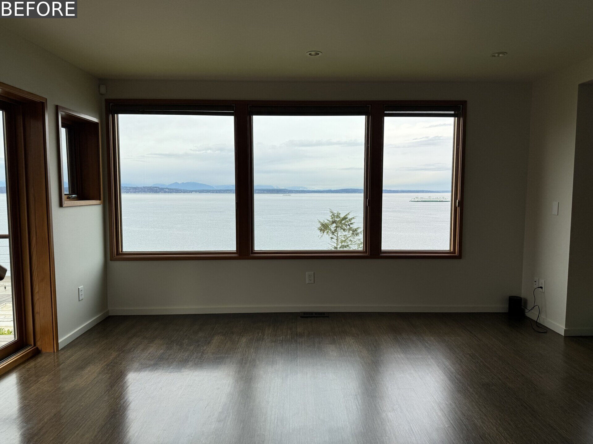 See the living room before renovation, with white walls, dark floors, timber-framed windows and an incredible Puget Sound view that had yet to become a bigger part of the room itself.