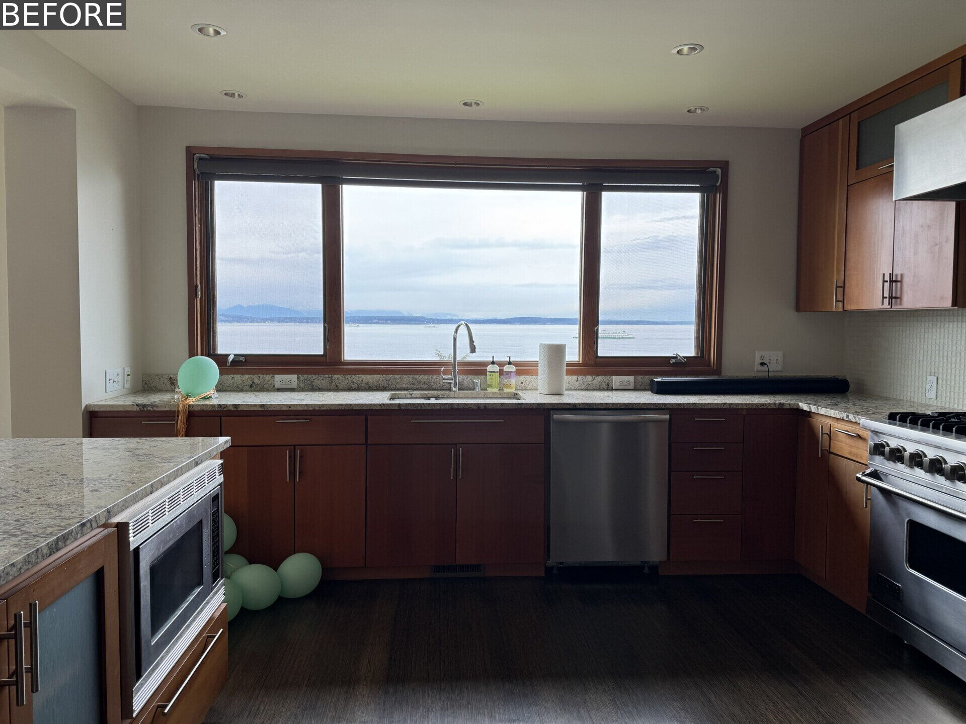 See the original kitchen at Alki Lookout, where dark timber cabinetry, granite counters and stainless-steel appliances occupied the prime window position overlooking Puget Sound.