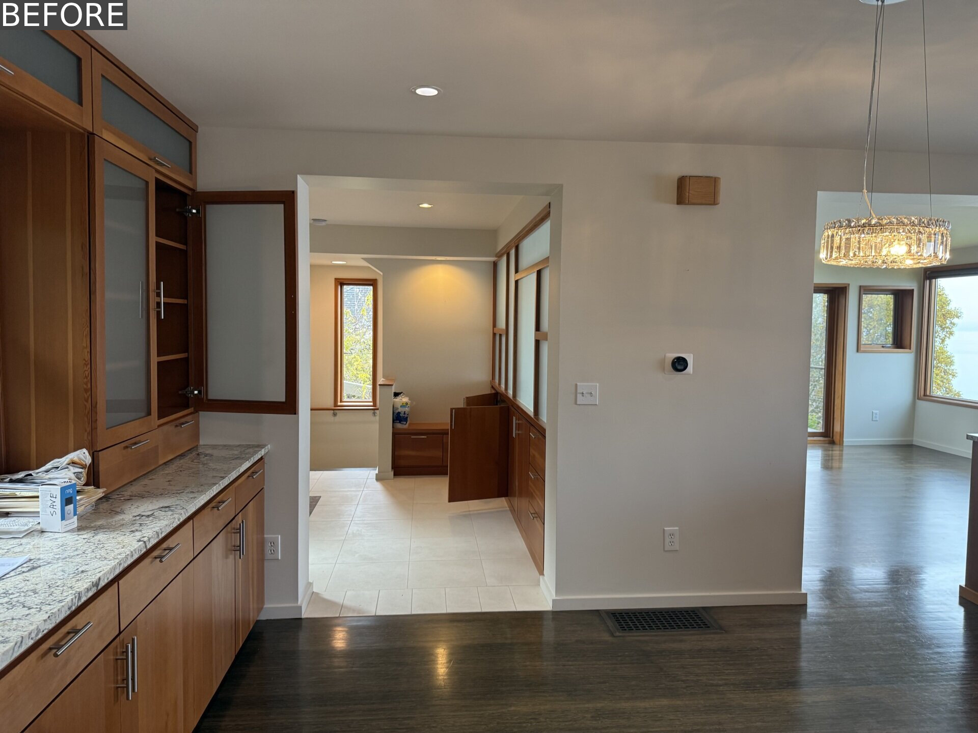 See how SHED transformed a wall of formal dark cabinetry into warm built-in storage with open display niches, yellow knobs, a bench with drawers and circular hooks for coats and bags.