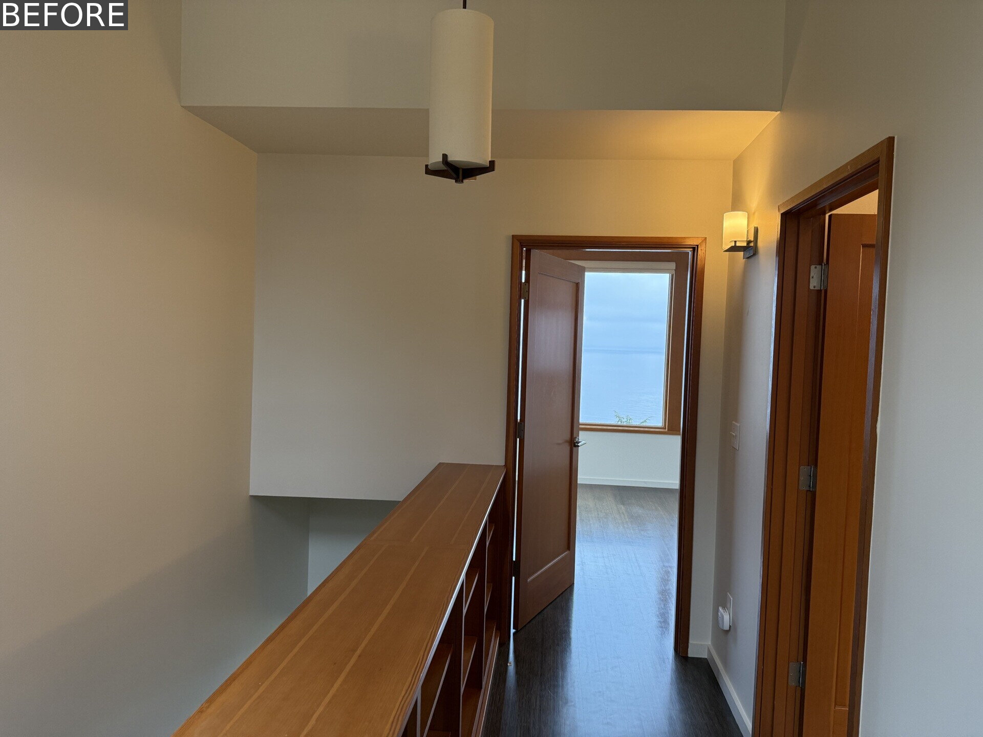 Explore the updated upper hallway, where pale timber flooring and a tall red-framed glazed transom pull light deeper into the house and create a clear view toward the bedroom and Puget Sound beyond.
