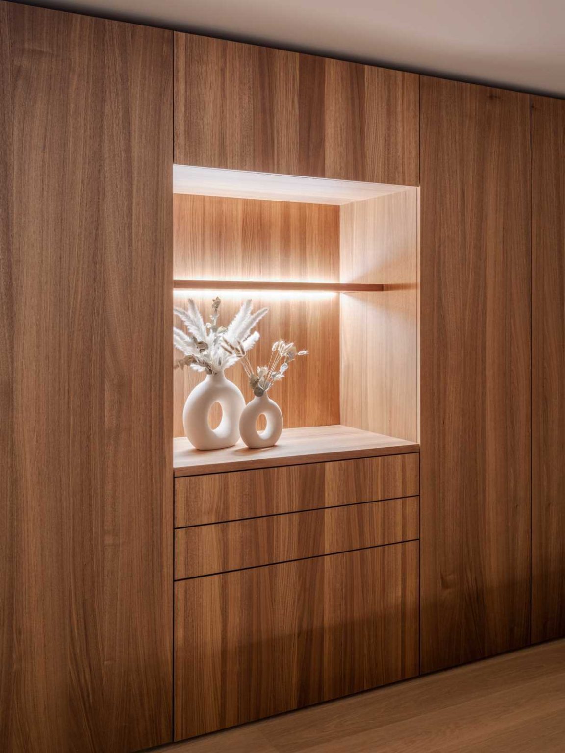 Warm wood cabinetry, hardwood floors and subtle hidden lighting create a cosy, modern primary bedroom in this Lausen, Switzerland home renovation.