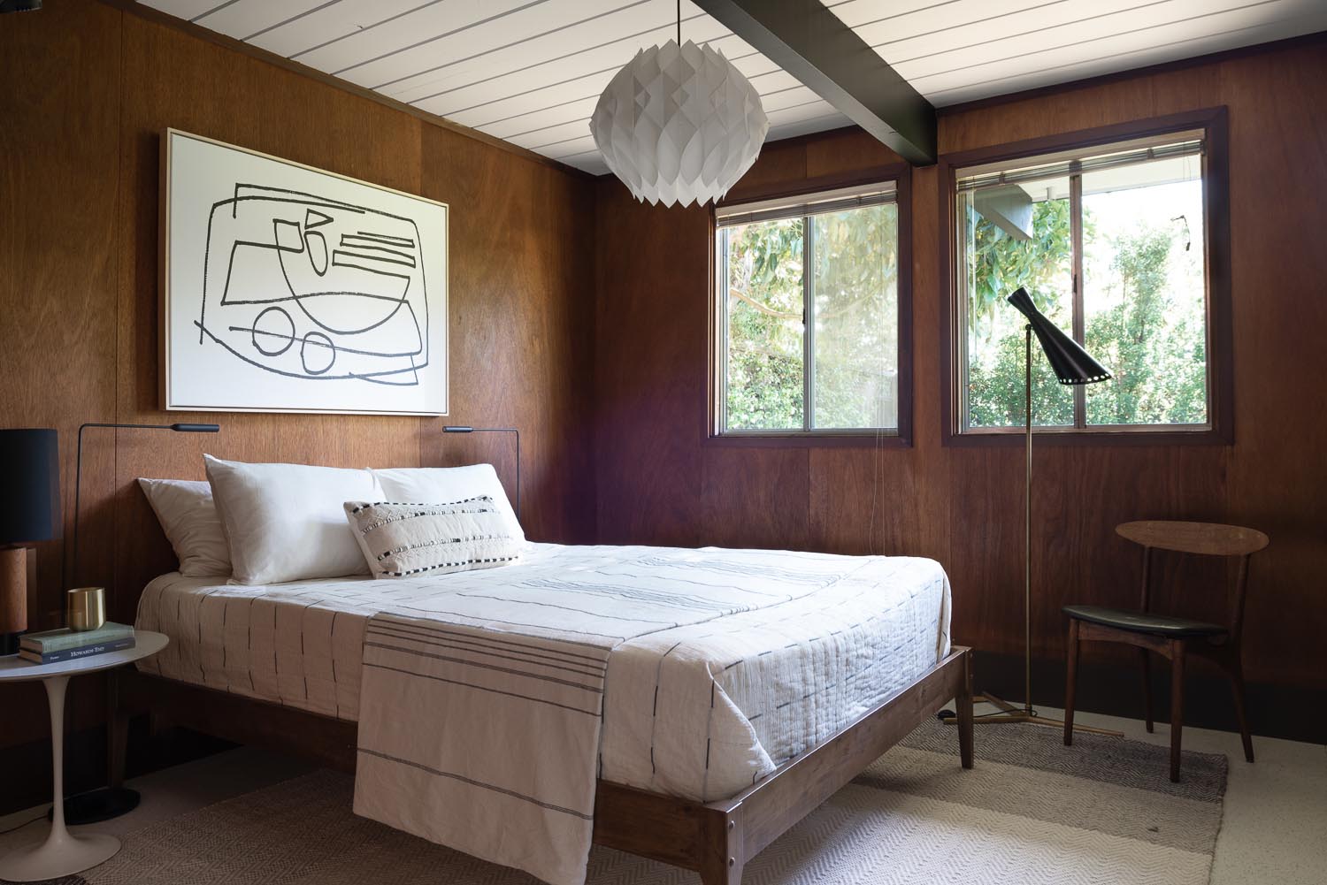 Step inside the bedrooms of this renovated Eichler house, featuring warm mahogany walls, mid-century furnishings, and artwork.