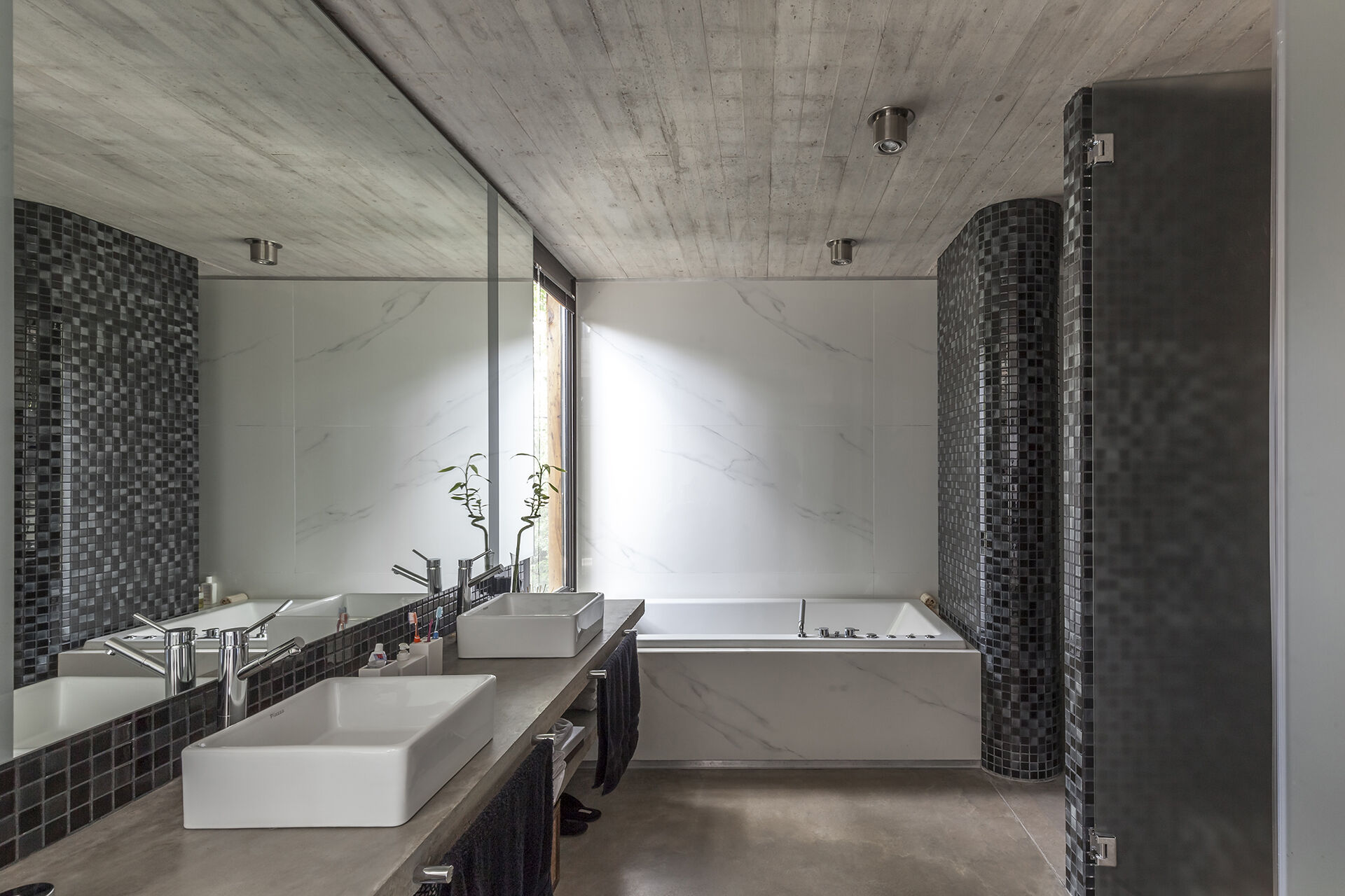 The bathroom at Casa Aranzazu pairs black and grey tiles with a bathtub positioned beside a window overlooking the outdoors.