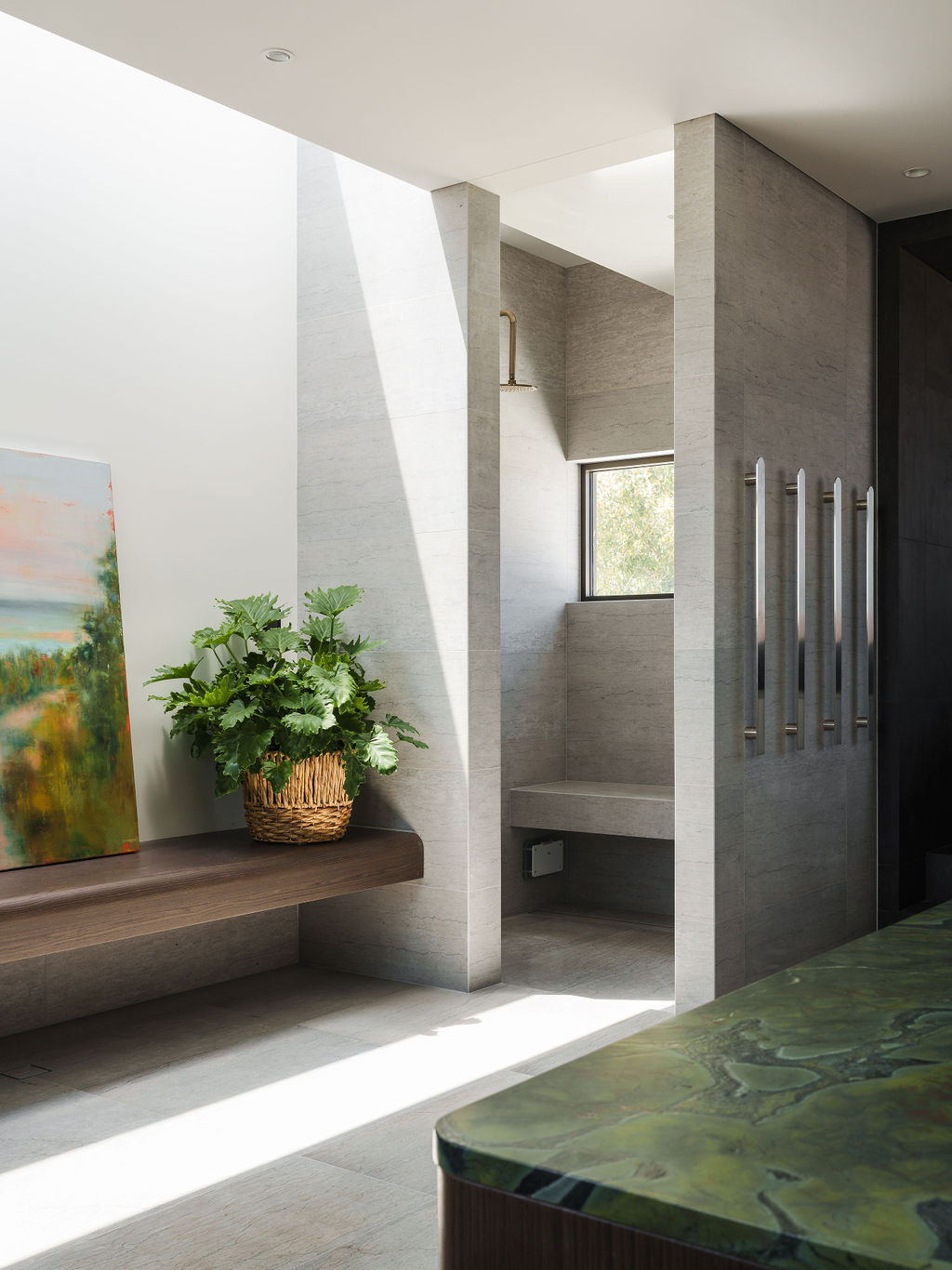 Inside the Mezzanine House bathroom, soft gray stone, dark surfaces, timber cabinetry and a green stone countertop create a calm contemporary space with a freestanding bathtub.