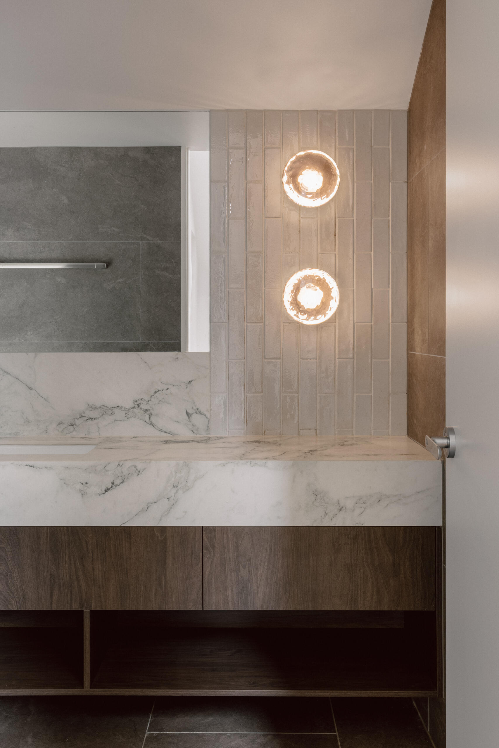 Explore the Yarra Valley House bathroom with white marble, dark wood cabinetry, grey tiles, warm round sconces and a large mirror.