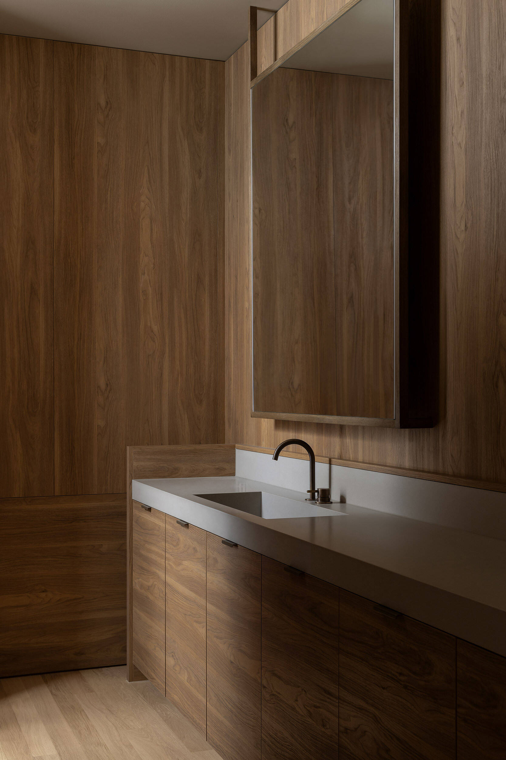 This bathroom has an oak palette with timber cabinetry, an integrated basin and a large mirrored cabinet, creating a warm, seamless interior.