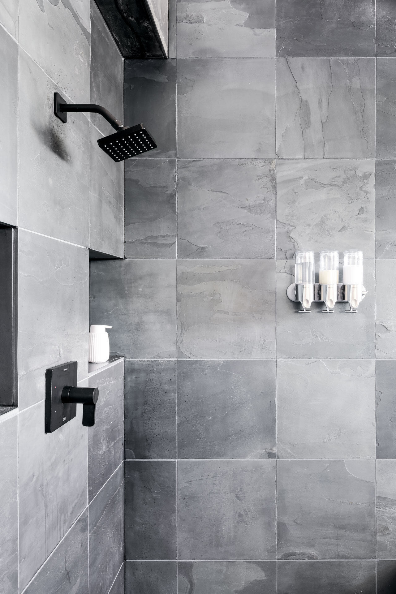 Large-format grey stone-look tiles, matte black shower fixtures, and recessed niches create a contemporary bathroom with a refined, minimalist material palette.