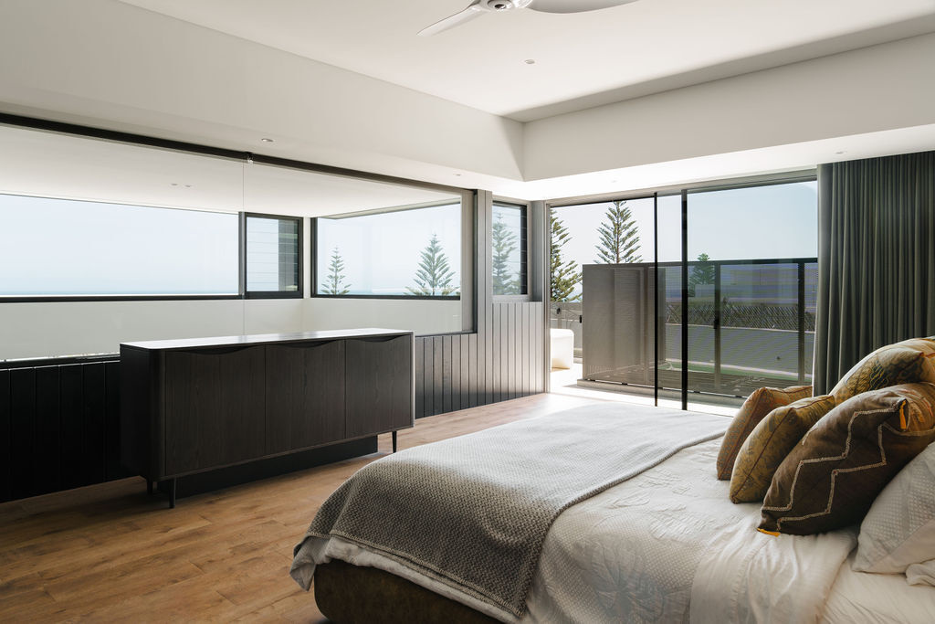 Dark timber paneling, warm wood floors and coastal views come together in the bedroom of Mezzanine House, a contemporary family home in Perth by Craig Steere Architects.