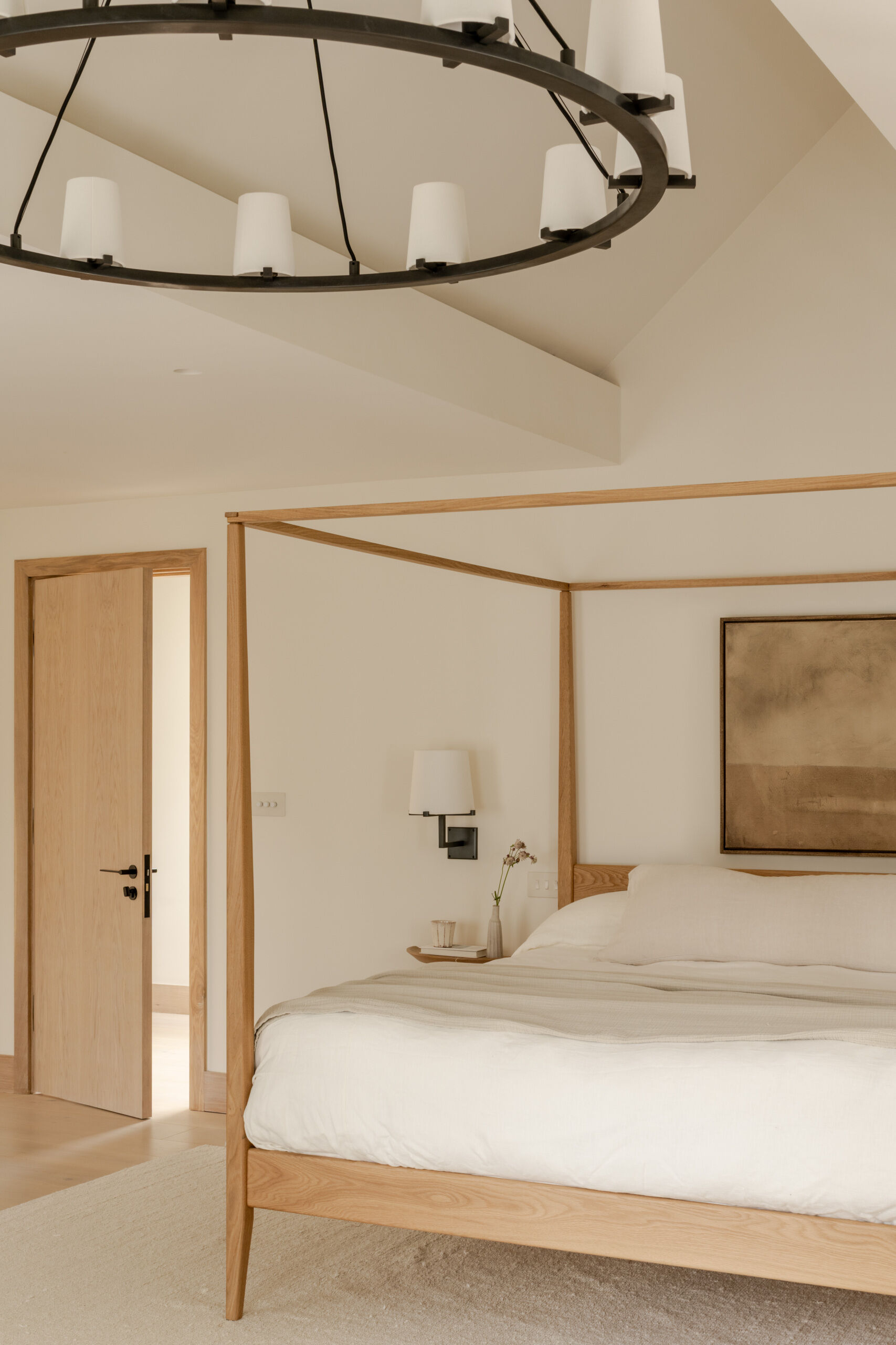 Step inside the primary bedroom at Thirsk Cottage, featuring soft neutral tones, pale oak flooring, warm wood, an ornate black fireplace and a slim four-poster bed.