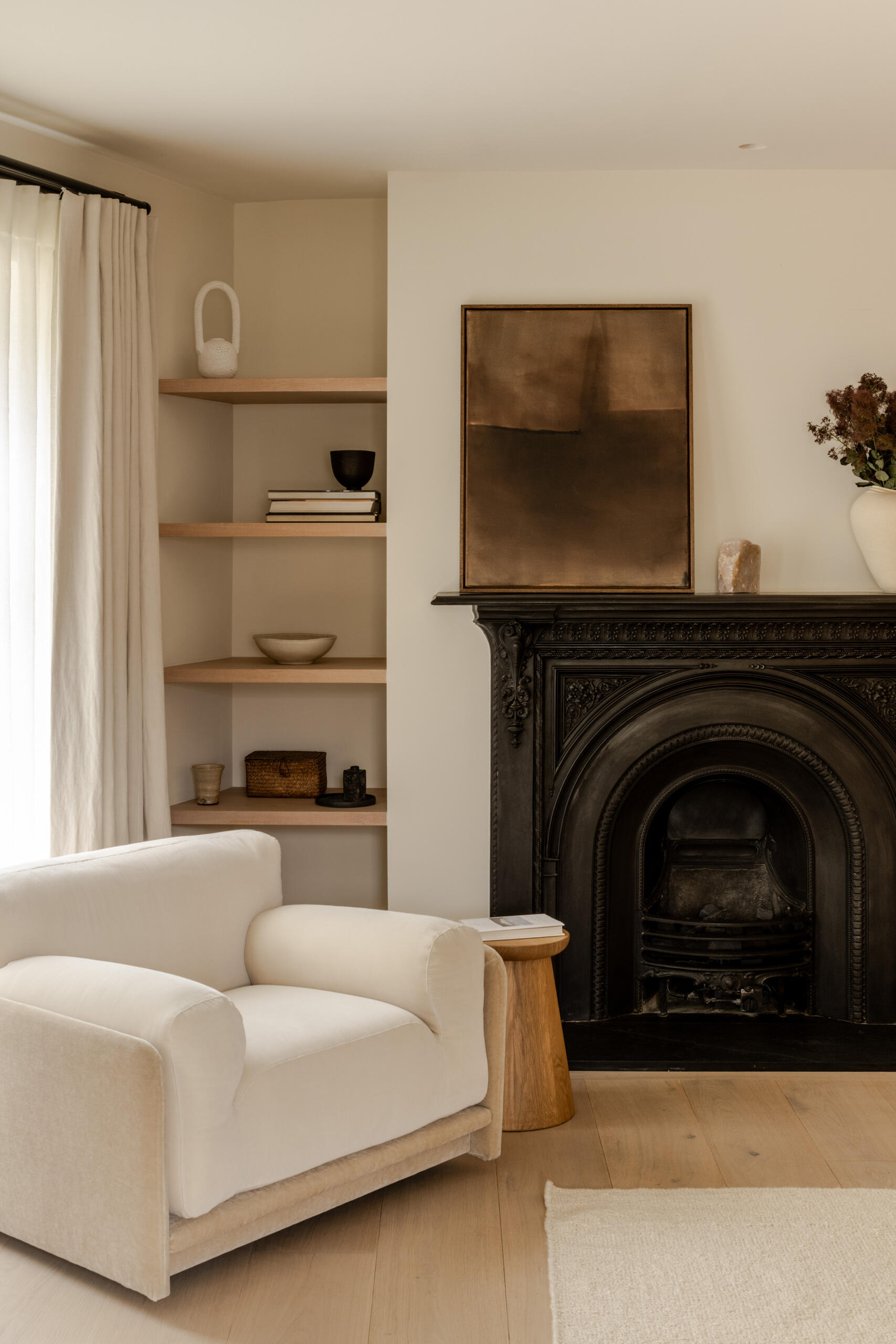 Step inside the primary bedroom at Thirsk Cottage, featuring soft neutral tones, pale oak flooring, warm wood, an ornate black fireplace and a slim four-poster bed.