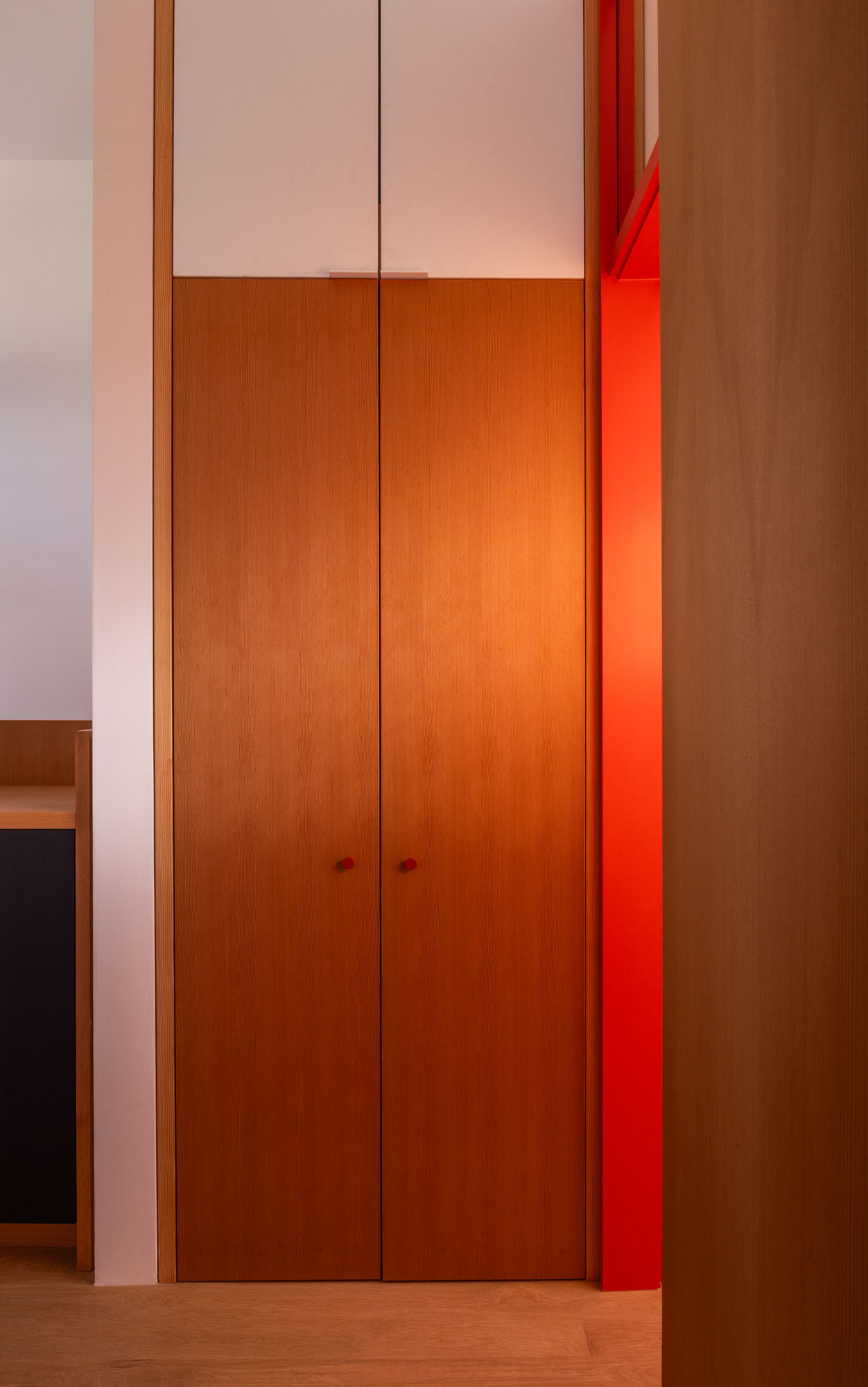 Explore the updated upper hallway, where pale timber flooring and a tall red-framed glazed transom pull light deeper into the house and create a clear view toward the bedroom and Puget Sound beyond.