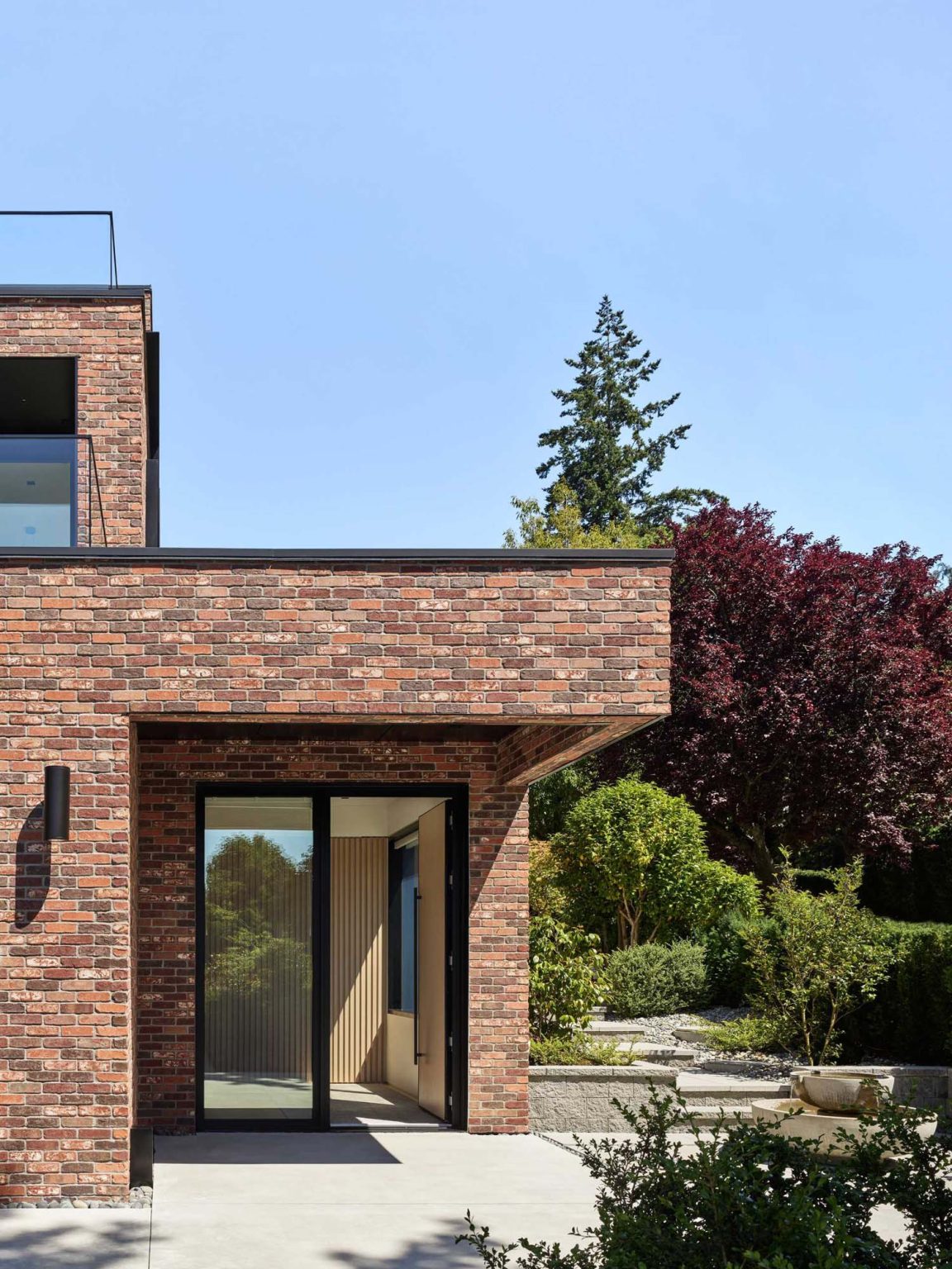 Nanton House has two entrances designed around its sloping site, including a lower garden-level foyer beneath a green roof and an upper entrance reached by a long steel bridge.
