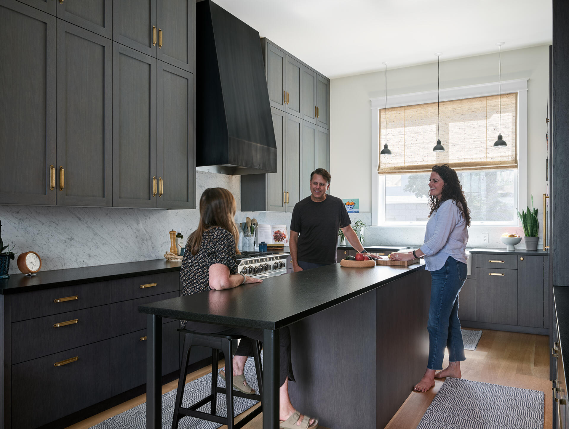 A warm San Francisco kitchen by Studio BBA features wood cabinetry, brass hardware, natural stone and a wide island designed for cooking, conversation and homework.