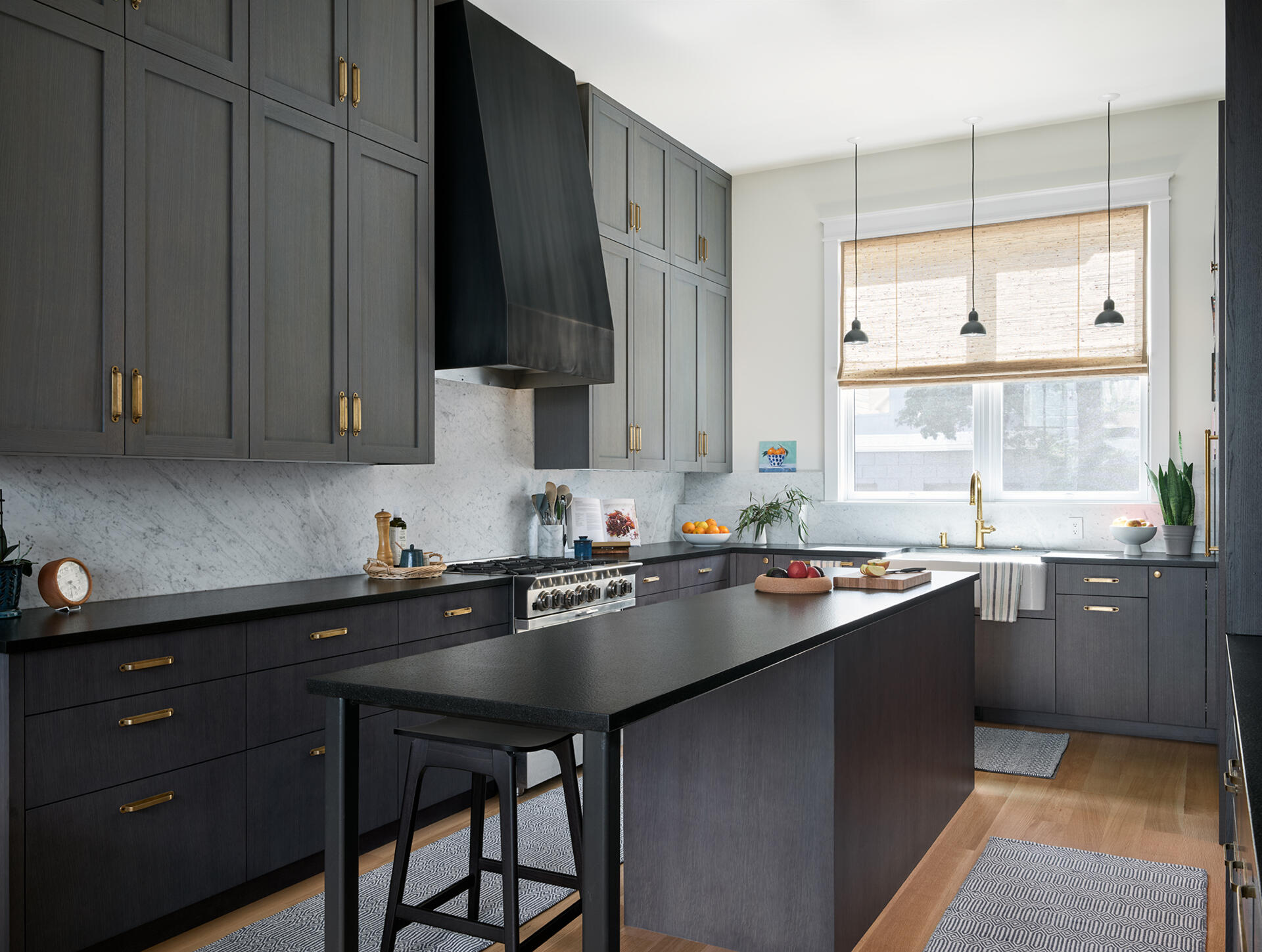 A warm San Francisco kitchen by Studio BBA features wood cabinetry, brass hardware, natural stone and a wide island designed for cooking, conversation and homework.