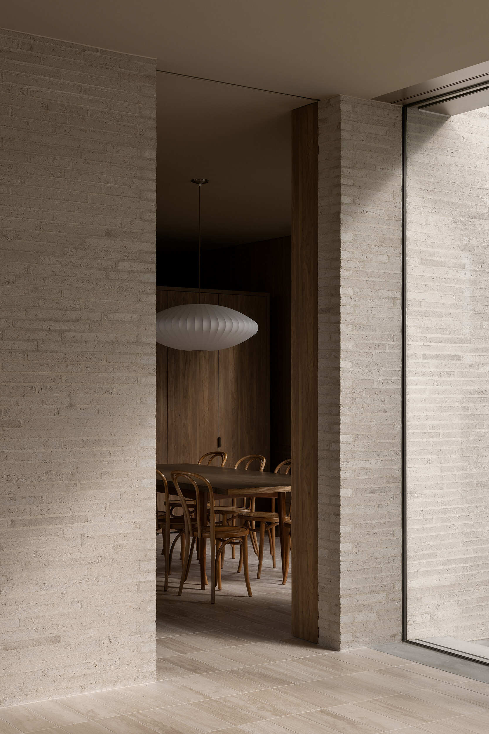 Warm timber cabinetry, bentwood chairs, a dark dining table and an oversized white pendant define Casa Piva’s dining area, with the larger internal courtyard bringing daylight and planting into the living spaces.