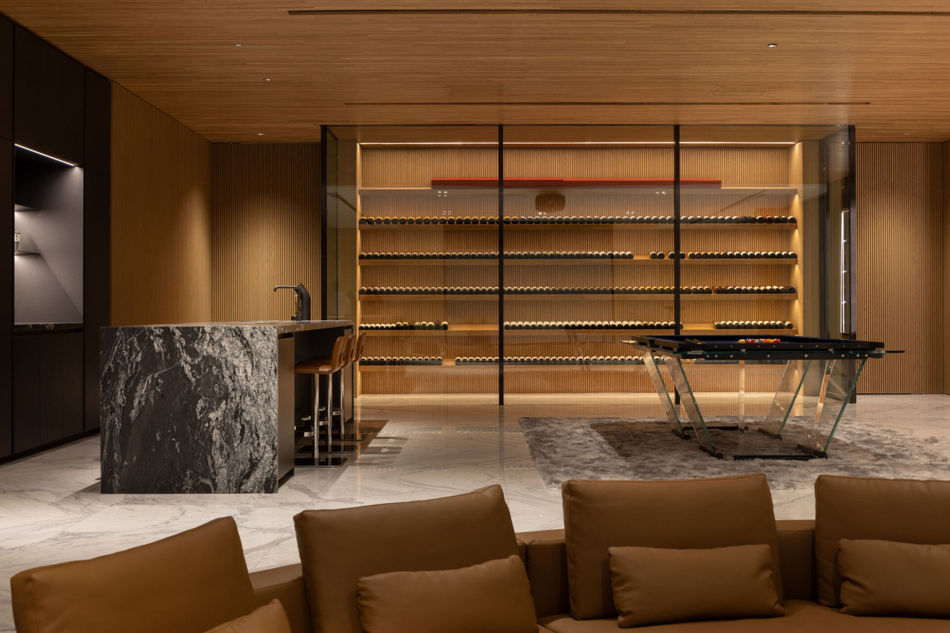 A sunken entertainment room with a wine cellar sits between two water gardens, with cascading water and trees visible through glass.
