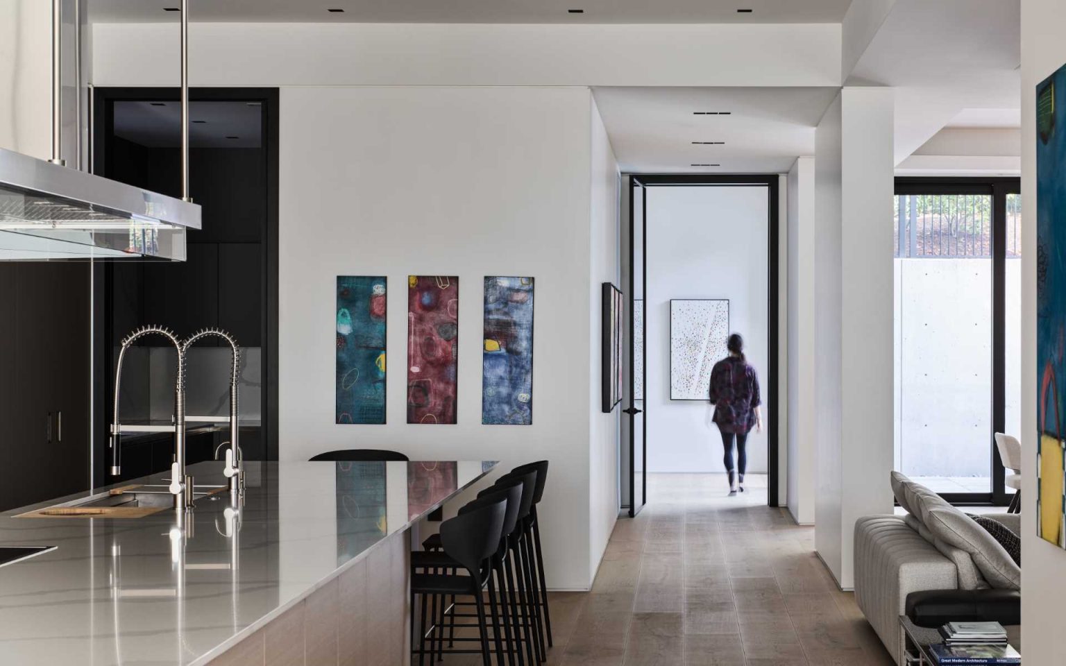 Grey cabinetry stretches along the kitchen and dining wall of Nanton House, contrasting with warm wood floors and millwork, while an island provides bar seating and garden views.