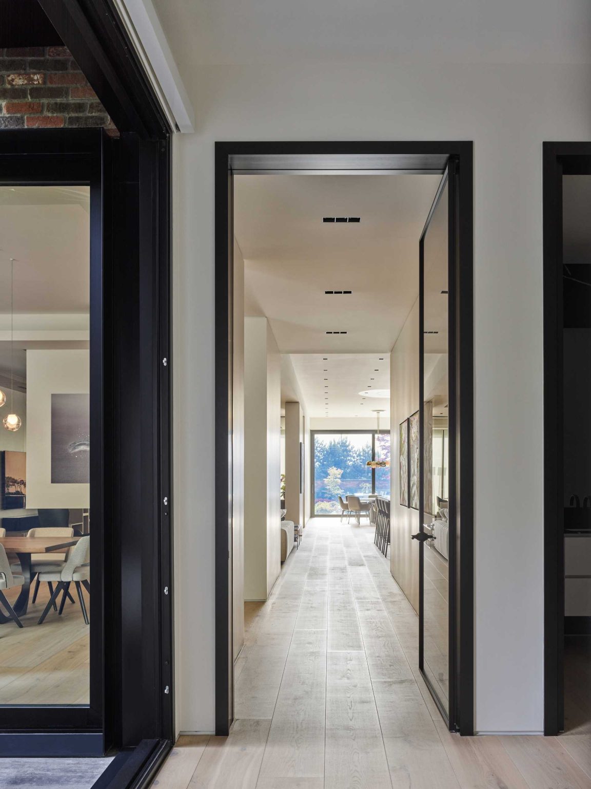 Grey cabinetry stretches along the kitchen and dining wall of Nanton House, contrasting with warm wood floors and millwork, while an island provides bar seating and garden views.