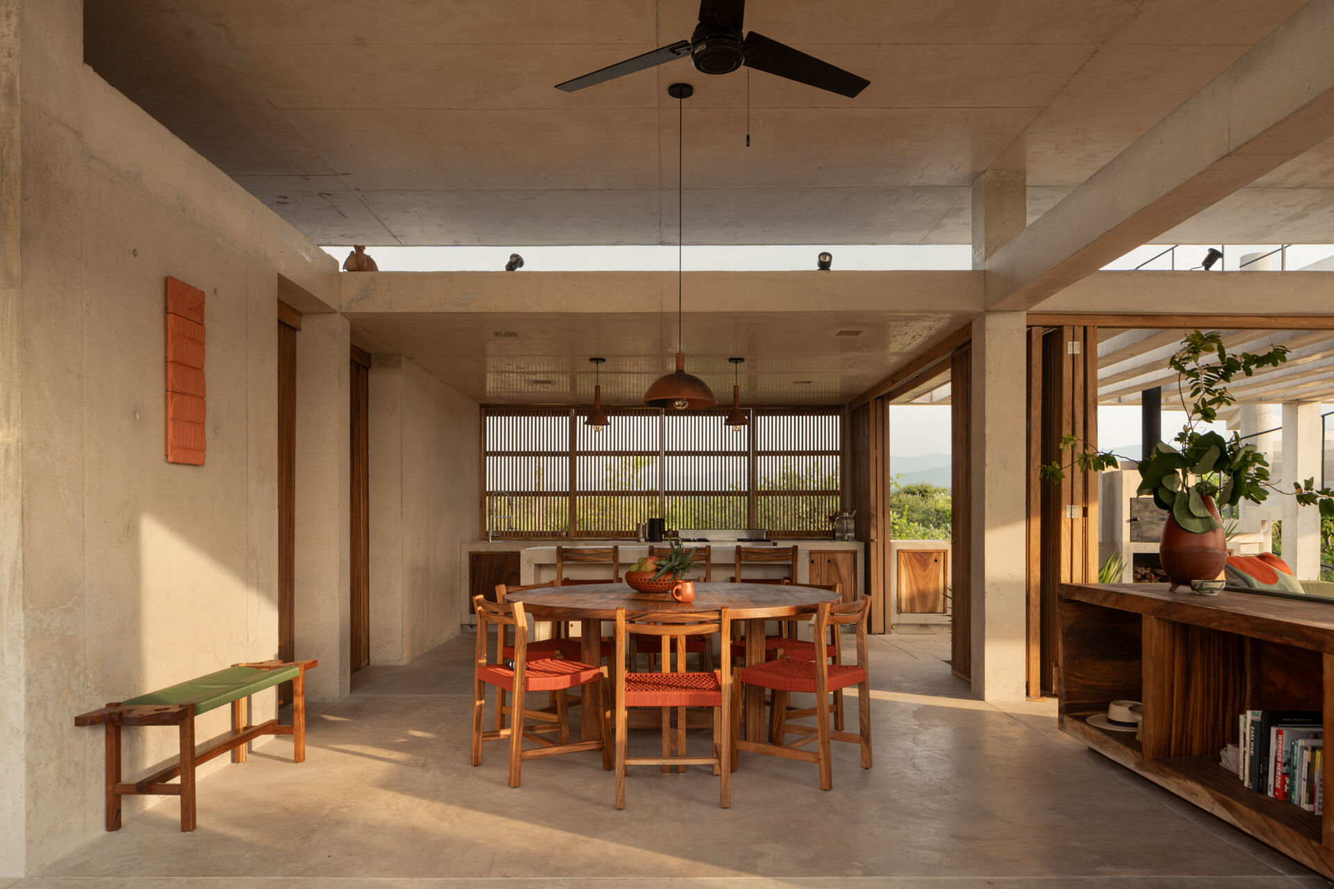 The interiors of Casa Cieno combine exposed concrete with warm timber, woven textures, terracotta accents and large openings overlooking the surrounding landscape.