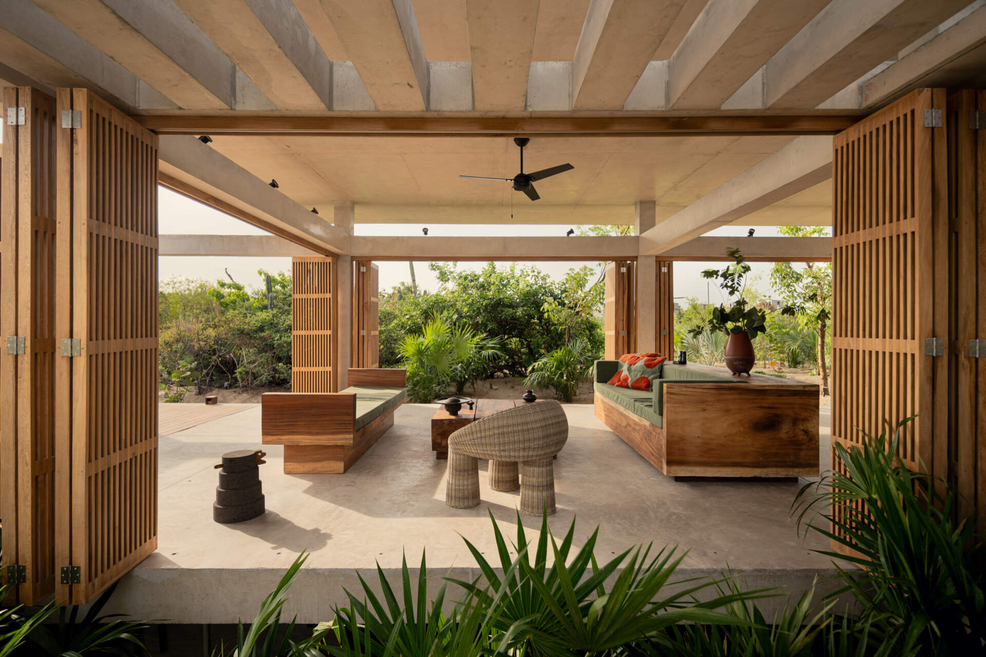 The interiors of Casa Cieno combine exposed concrete with warm timber, woven textures, terracotta accents and large openings overlooking the surrounding landscape.