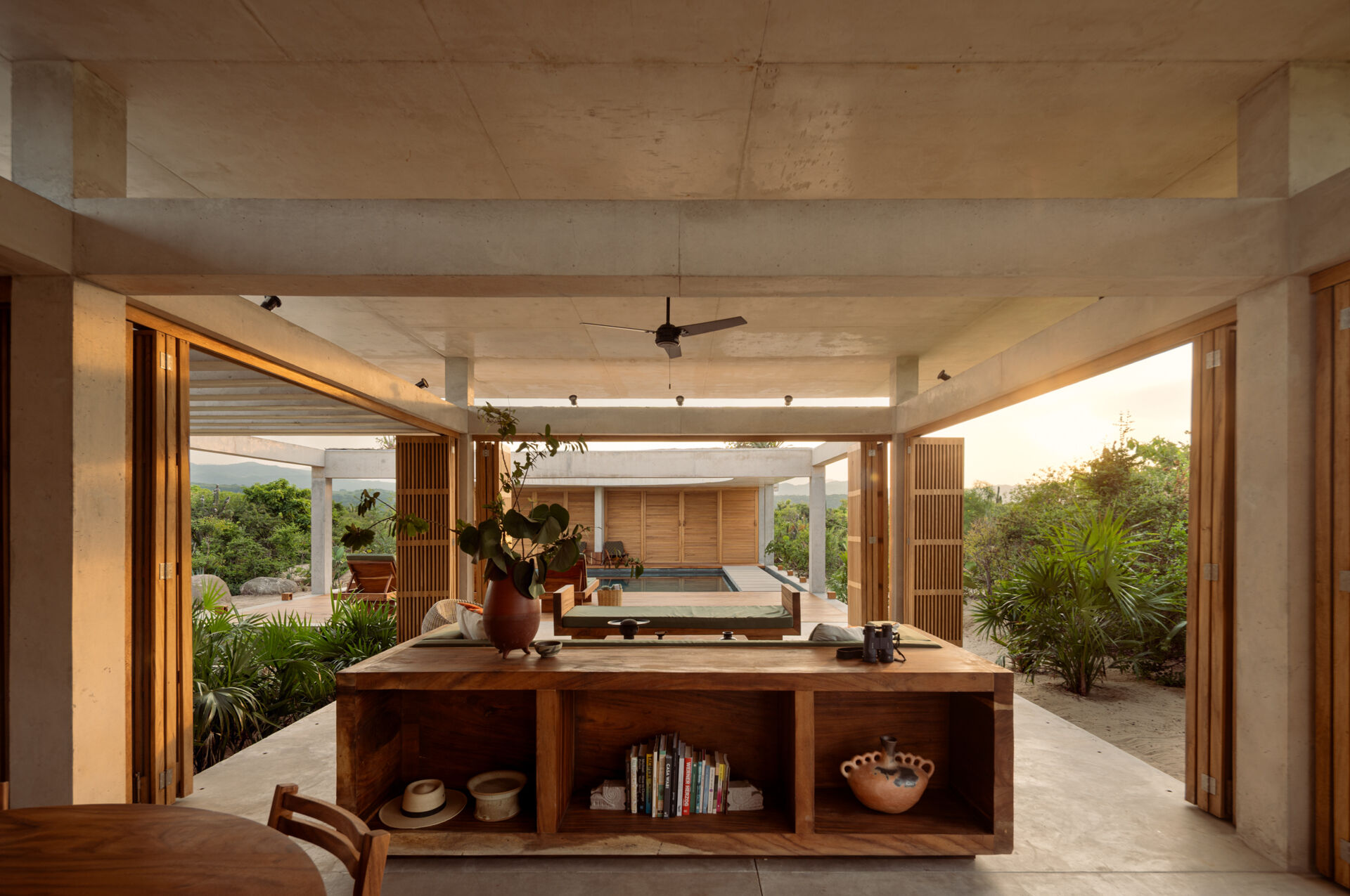 The interiors of Casa Cieno combine exposed concrete with warm timber, woven textures, terracotta accents and large openings overlooking the surrounding landscape.