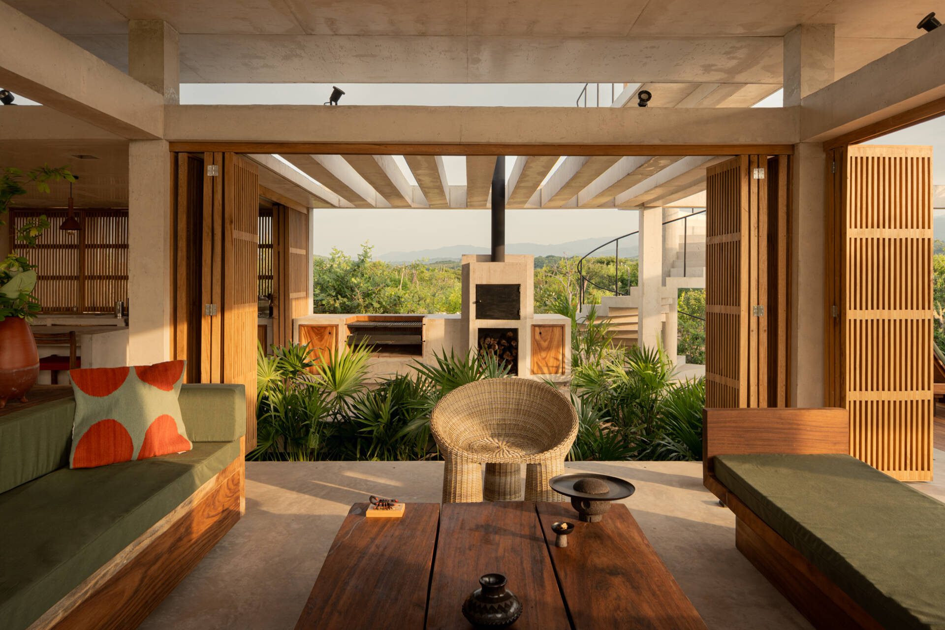 The interiors of Casa Cieno combine exposed concrete with warm timber, woven textures, terracotta accents and large openings overlooking the surrounding landscape.