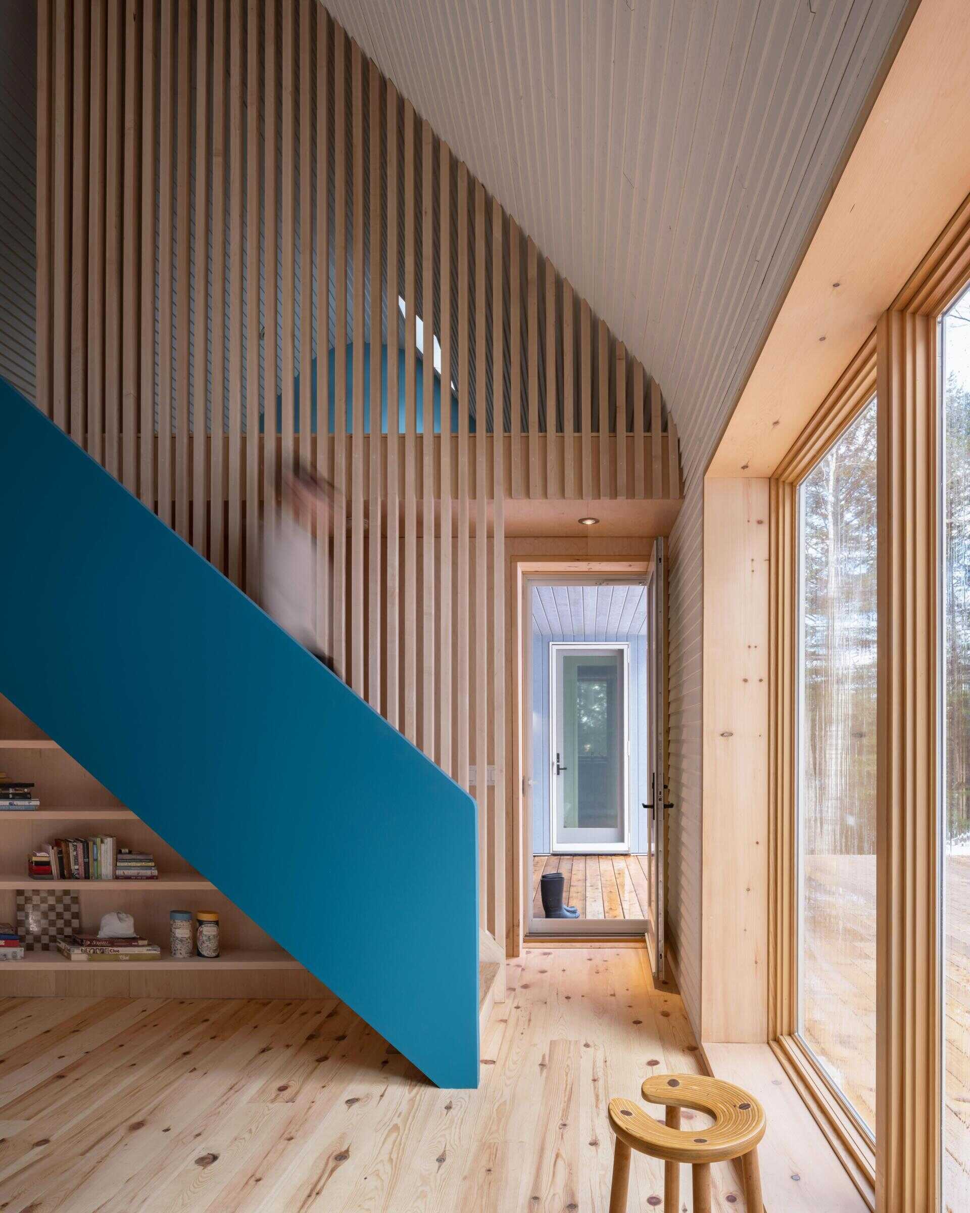 A modern cottage loft featuring a curved white timber ceiling, blue painted gable wall, maple slat screen, and sculptural staircase within a warm minimalist interior.