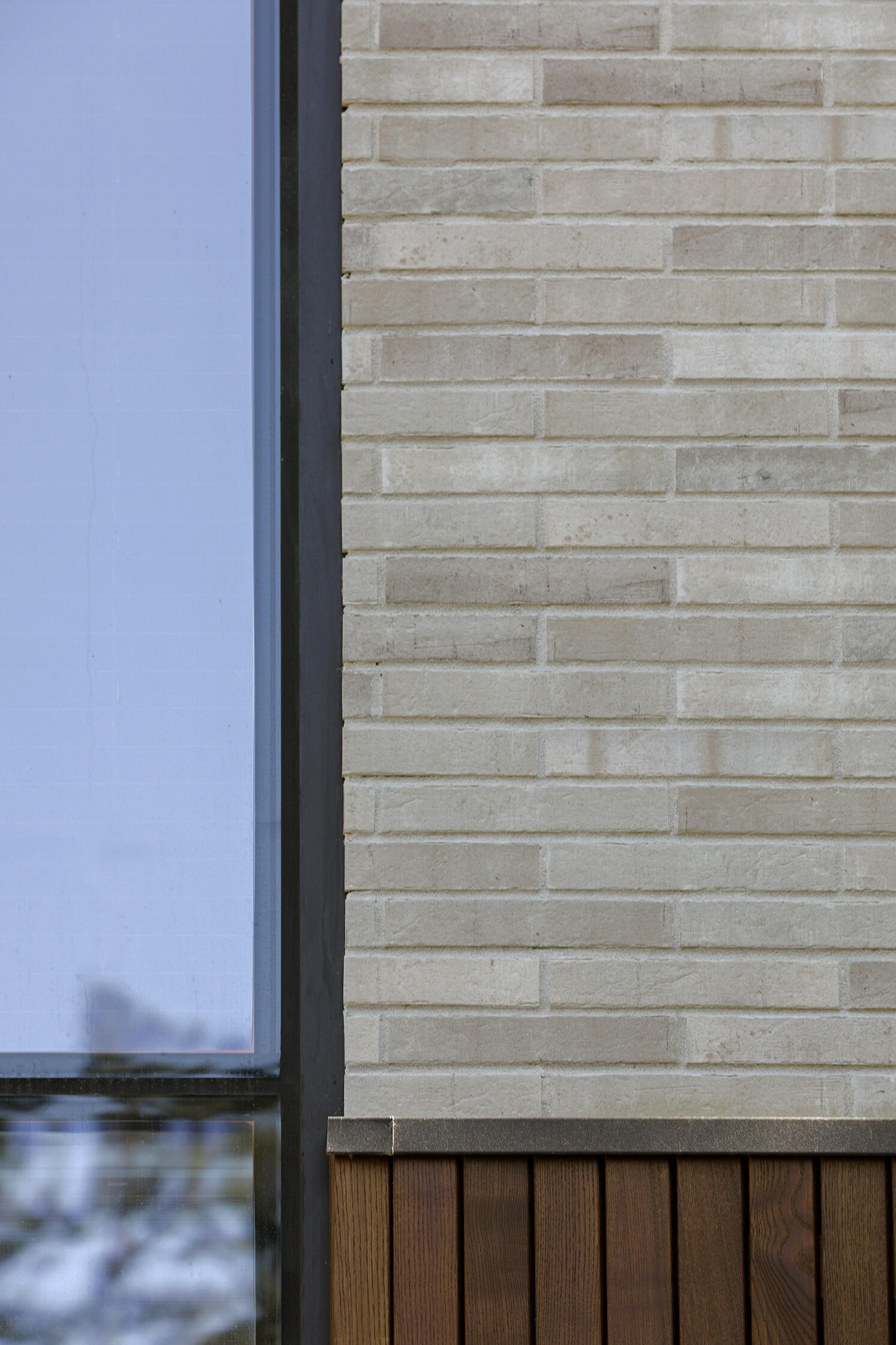 Dark vertical timber and light horizontal façade tiles distinguish the two intersecting volumes of The Intersecting House, creating a clear contrast across the contemporary forest home.