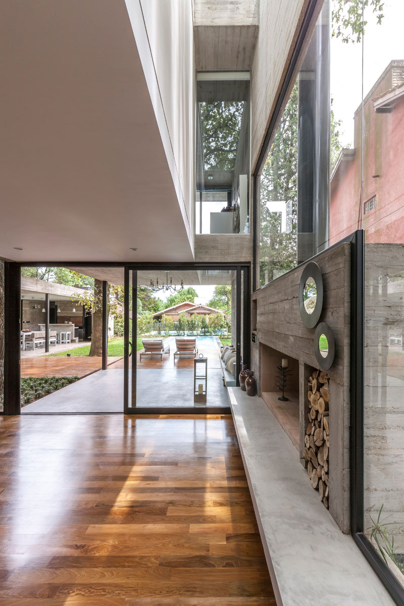 Explore the modern living room of Casa Aranzazu, where exposed concrete, warm wood shelving, large windows and a built-in fireplace create a clean yet inviting interior.