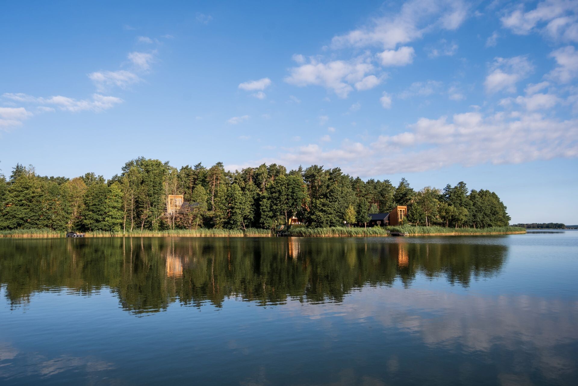 Explore the contemporary architecture of Kalbornia Mazury, featuring light wooden facades, dark private volumes and expansive glazing that opens the homes towards the Polish lake and forest.