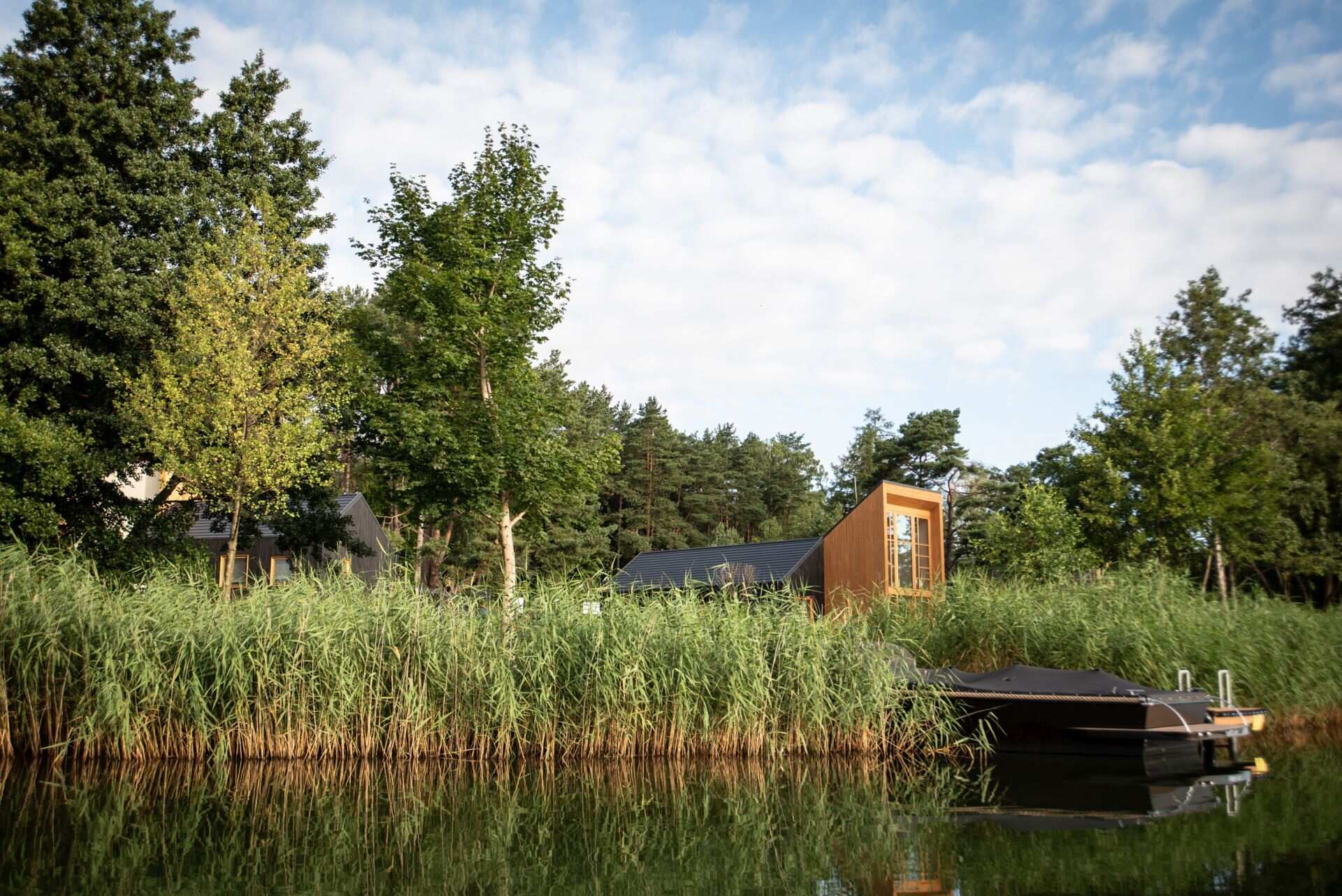 Explore the contemporary architecture of Kalbornia Mazury, featuring light wooden facades, dark private volumes and expansive glazing that opens the homes towards the Polish lake and forest.