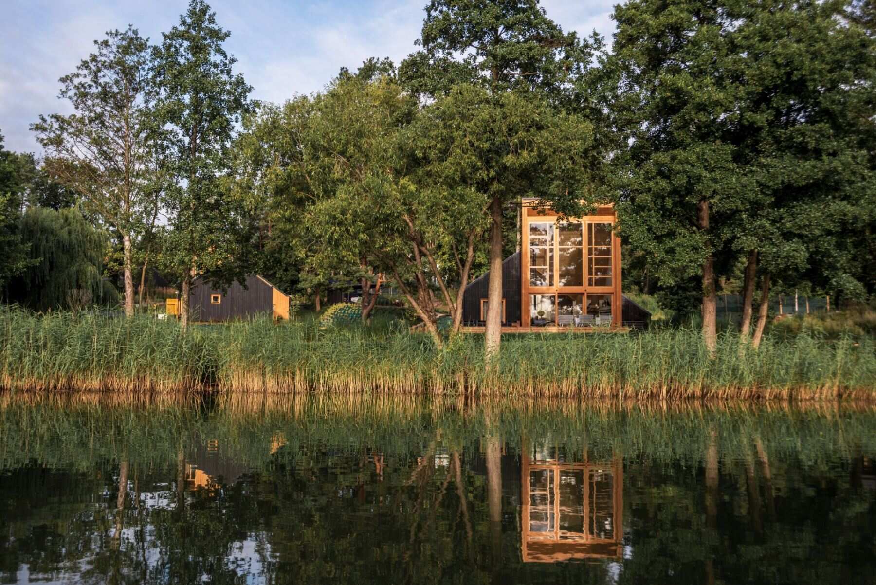 Explore the contemporary architecture of Kalbornia Mazury, featuring light wooden facades, dark private volumes and expansive glazing that opens the homes towards the Polish lake and forest.