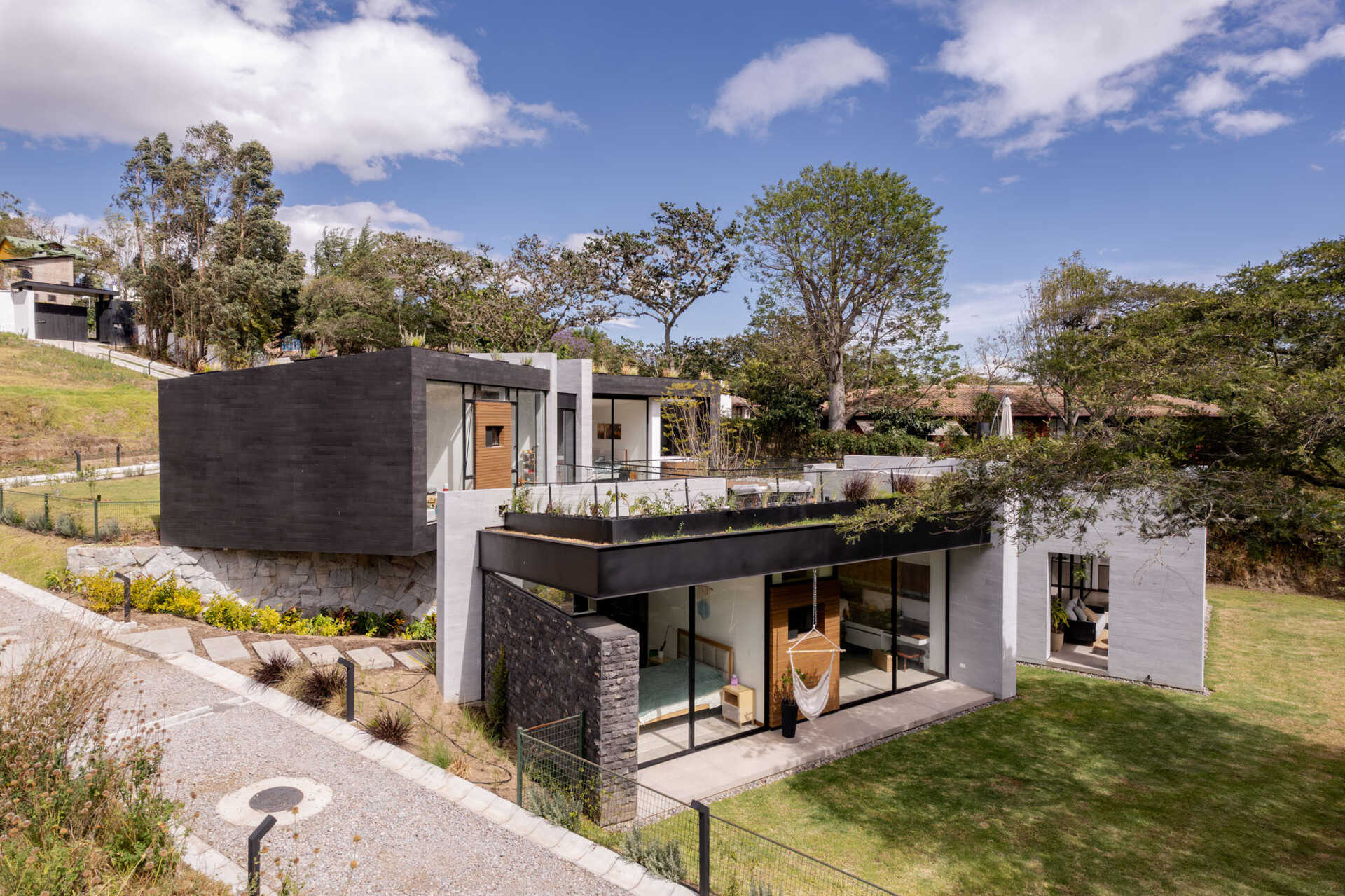 Explore a contemporary house in Puembo, Ecuador, with angular architecture, grass-covered roof terraces, a planted central courtyard, and sheltered outdoor living spaces. Designed by A1 Arquitectura Avanzada, the home combines pale walls, dark roof edges, wood-toned panels, and expansive glazing.