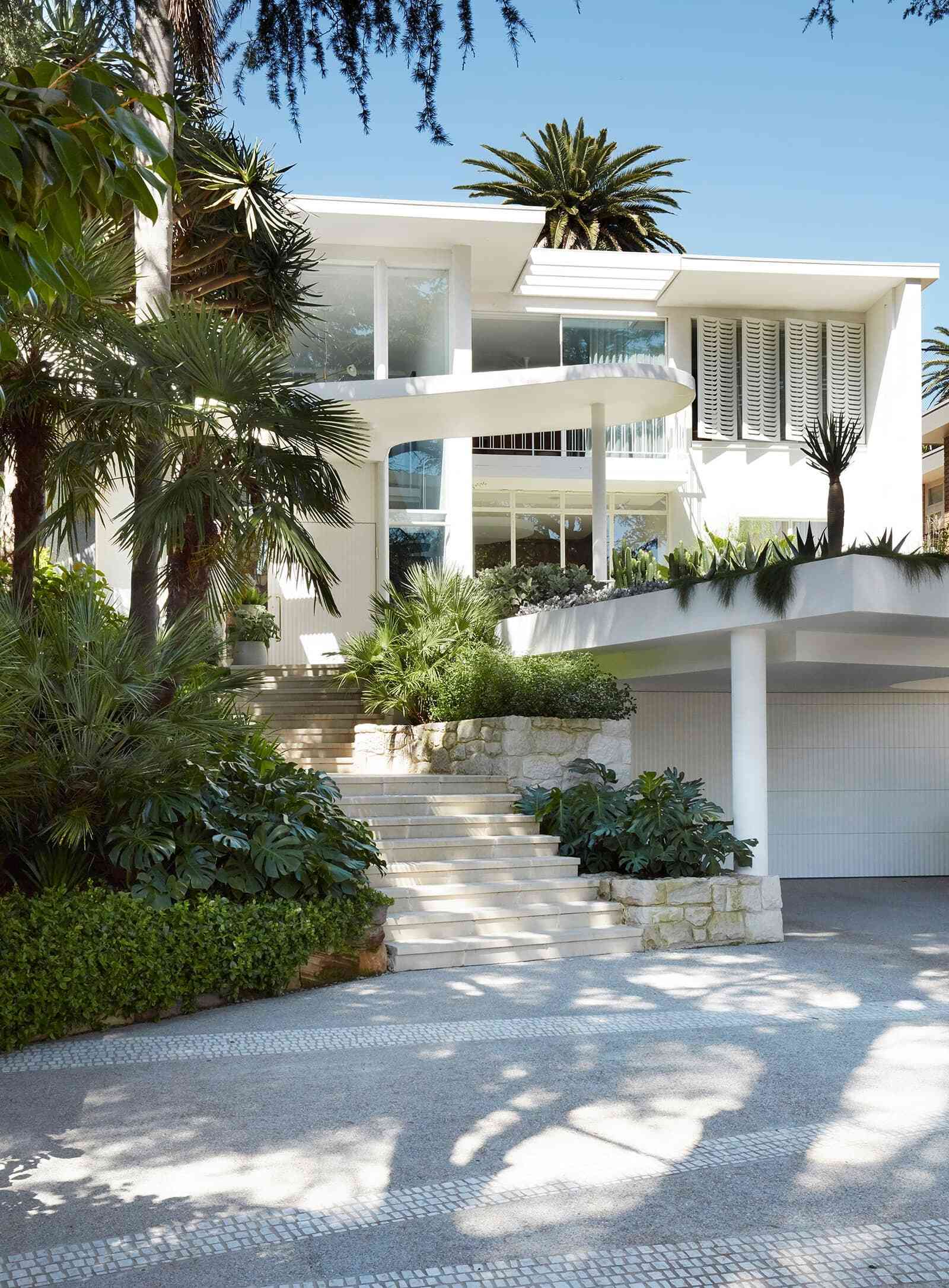 A sculptural curved concrete awning inspired by Oscar Niemeyer welcomes visitors to this Bellevue Hill modernist home, paired with a large white pivot front door.