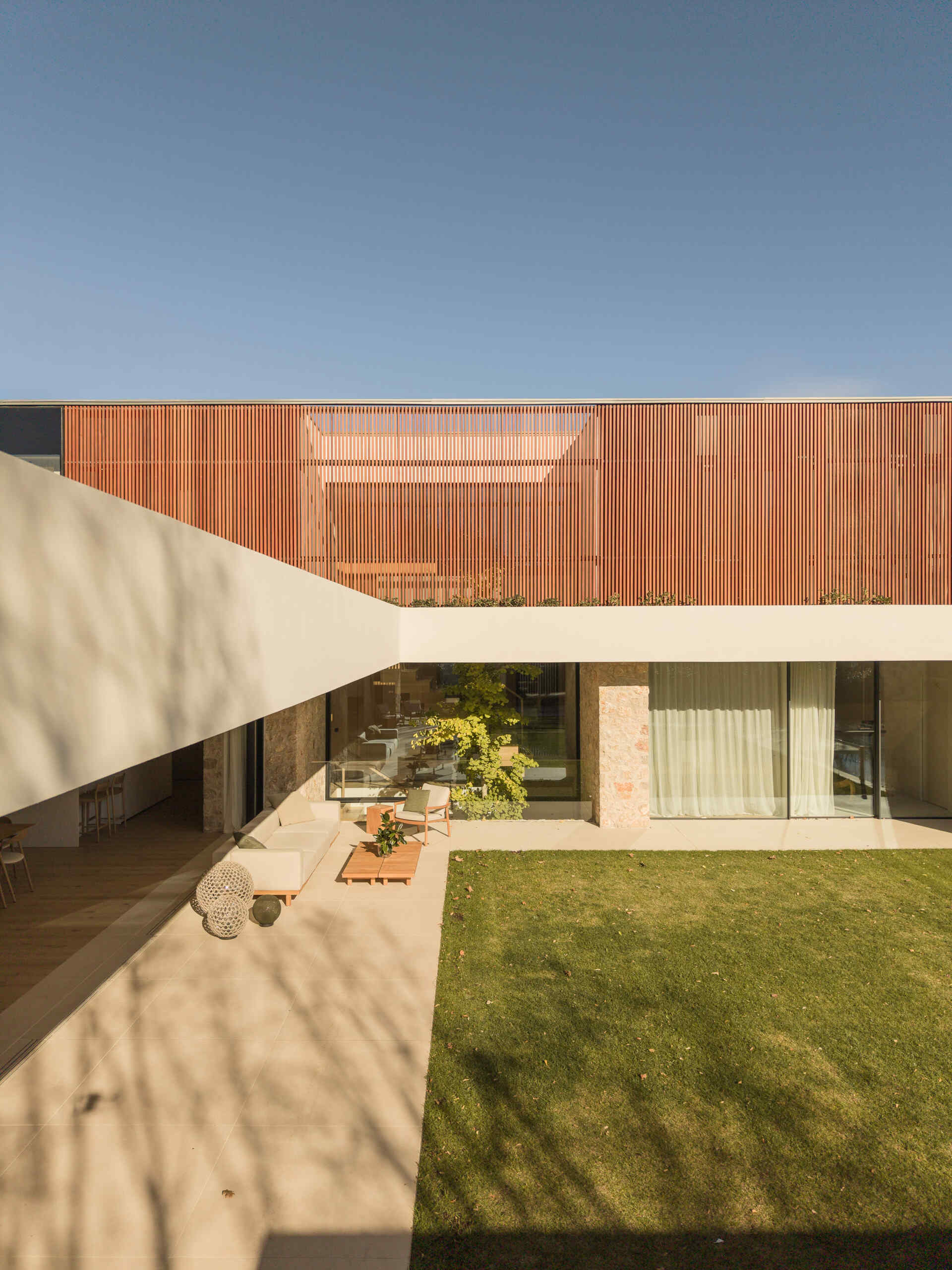 Vertical wooden shutters filter light and views around the upper floor of House 2194 in Olot, Spain. A planted roof adds greenery outside the private rooms of this home by Nordest Architecture SLP.